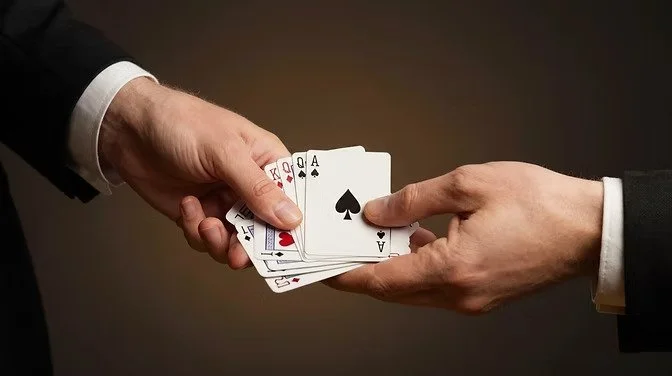 Two people exchanging a hand of playing cards, including aces, kings, queens, and a jack.