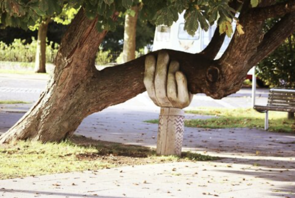A large tree with a carved wooden hand sculpture that appears to hold the trunk.