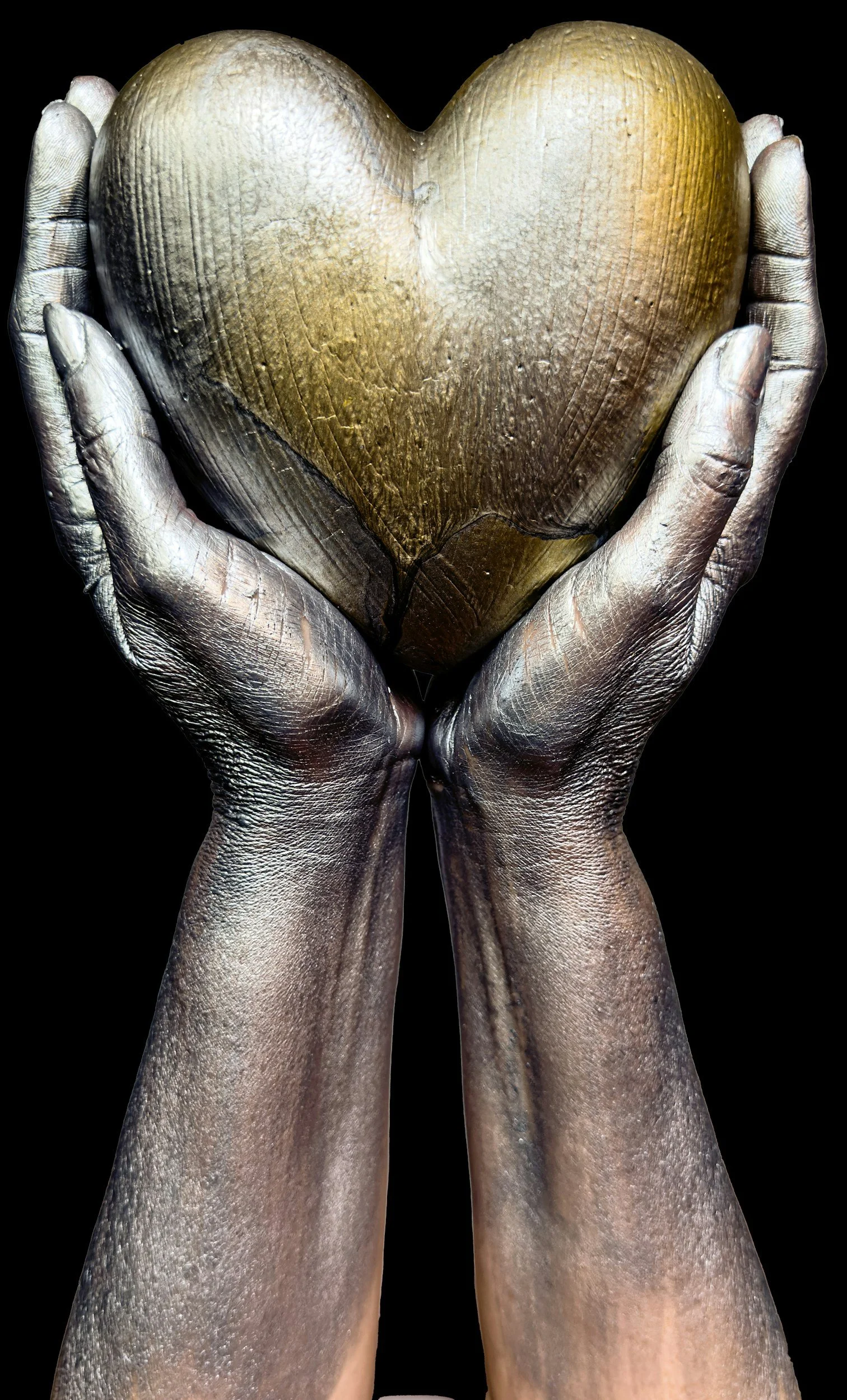 Two hands painted silver holding a gold heart-shaped object against a black background.