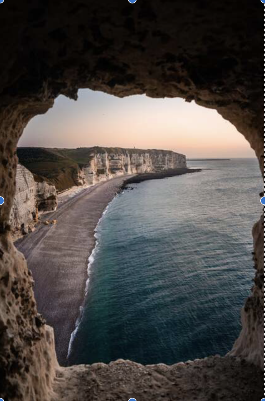 A view of a coastal cliff with white chalk formations and a sandy beach, seen through a natural rock window during sunset.