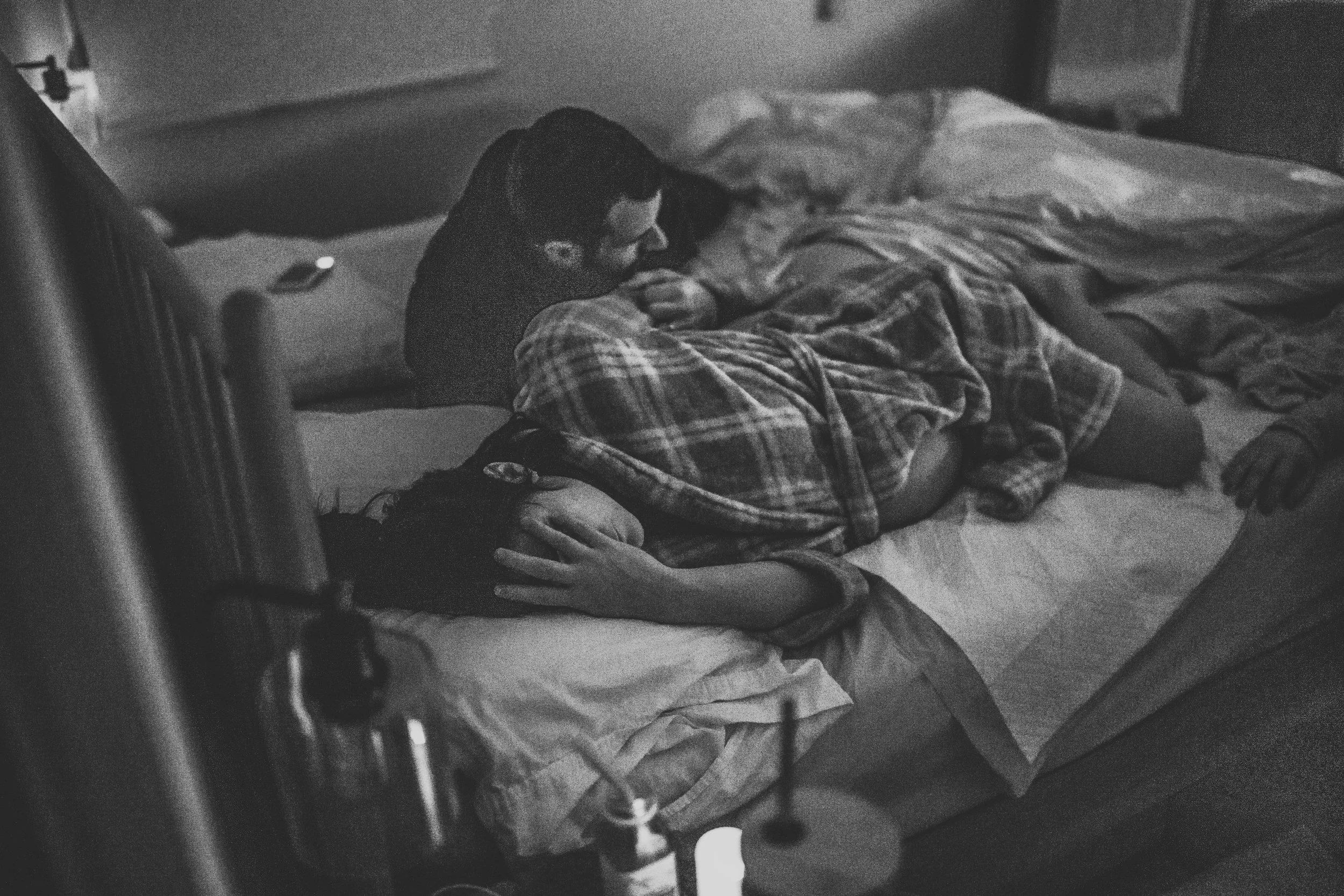A person laying in bed, resting their head on a pillow, with a blanket covering part of their body. The room appears dimly lit.