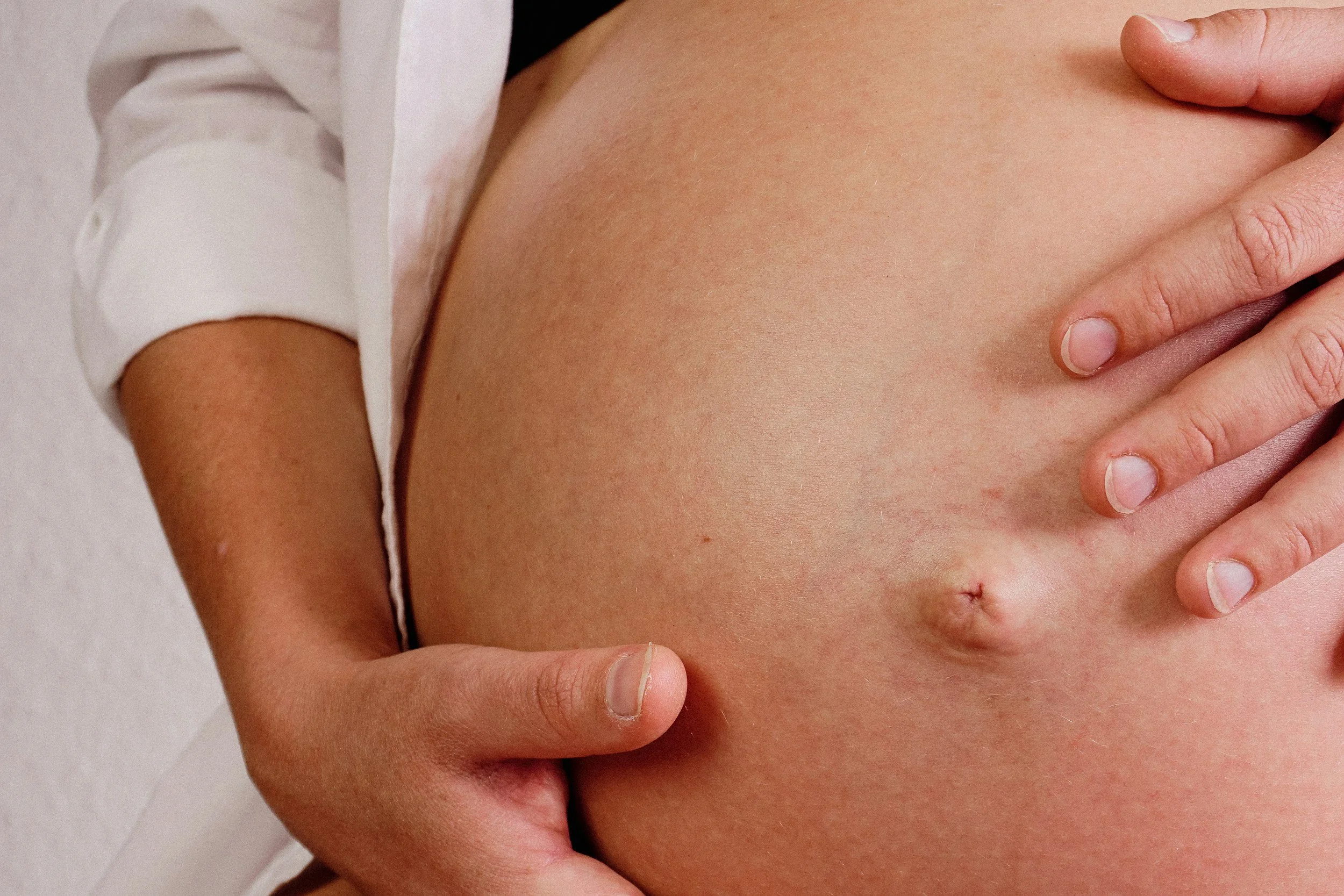 Close-up of a pregnant woman lying down, with her hand gently resting on her belly, in soft natural light.