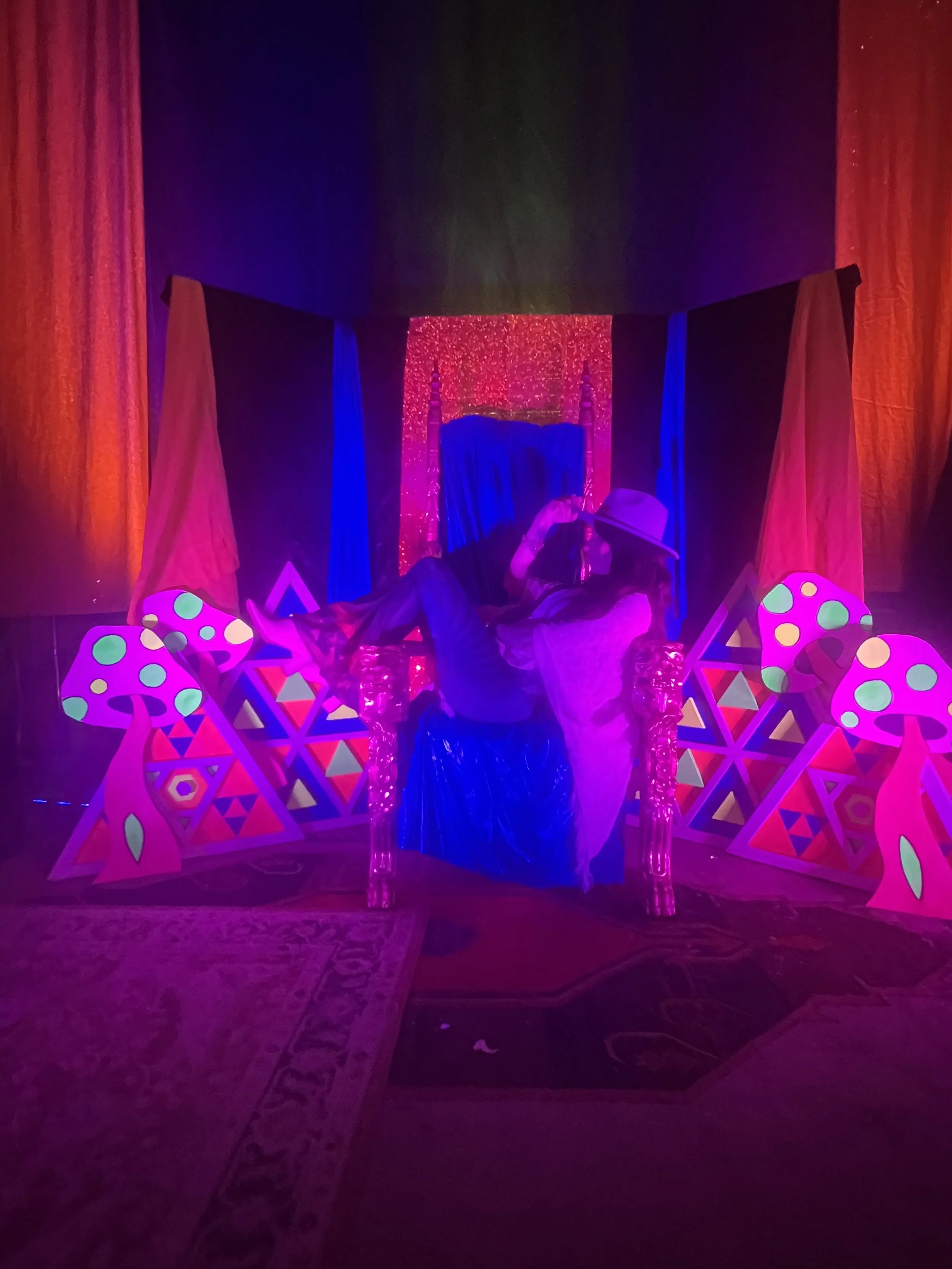 A colorful, neon-lit birthday party setup with a chair, decorations, and a person wearing a hat taking a photo.