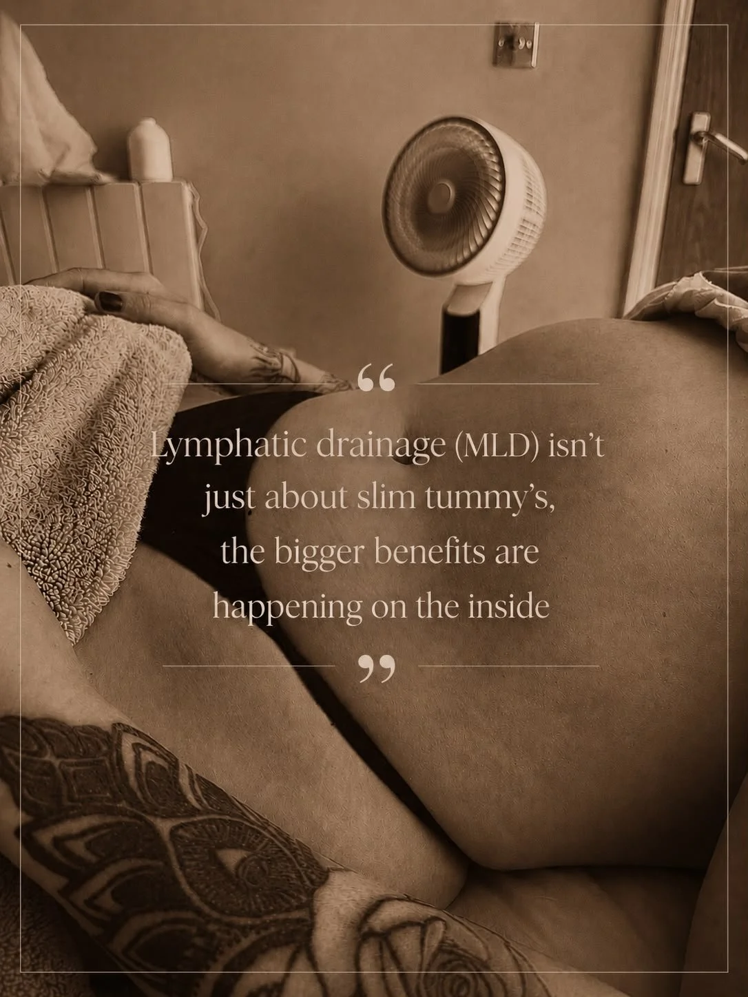 A woman lying on a bed with a blanket, with a tattoo on her forearm, and a plastic fan nearby, in a room with a door and wall-mounted electrical outlets.