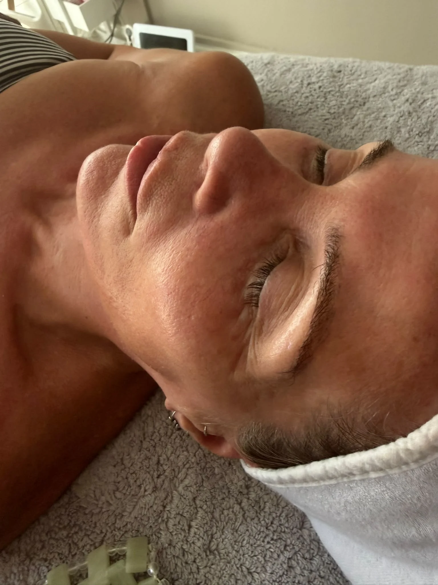 Person lying on a bed with eyes closed, covered with a white towel, resting face down on a soft blanket.