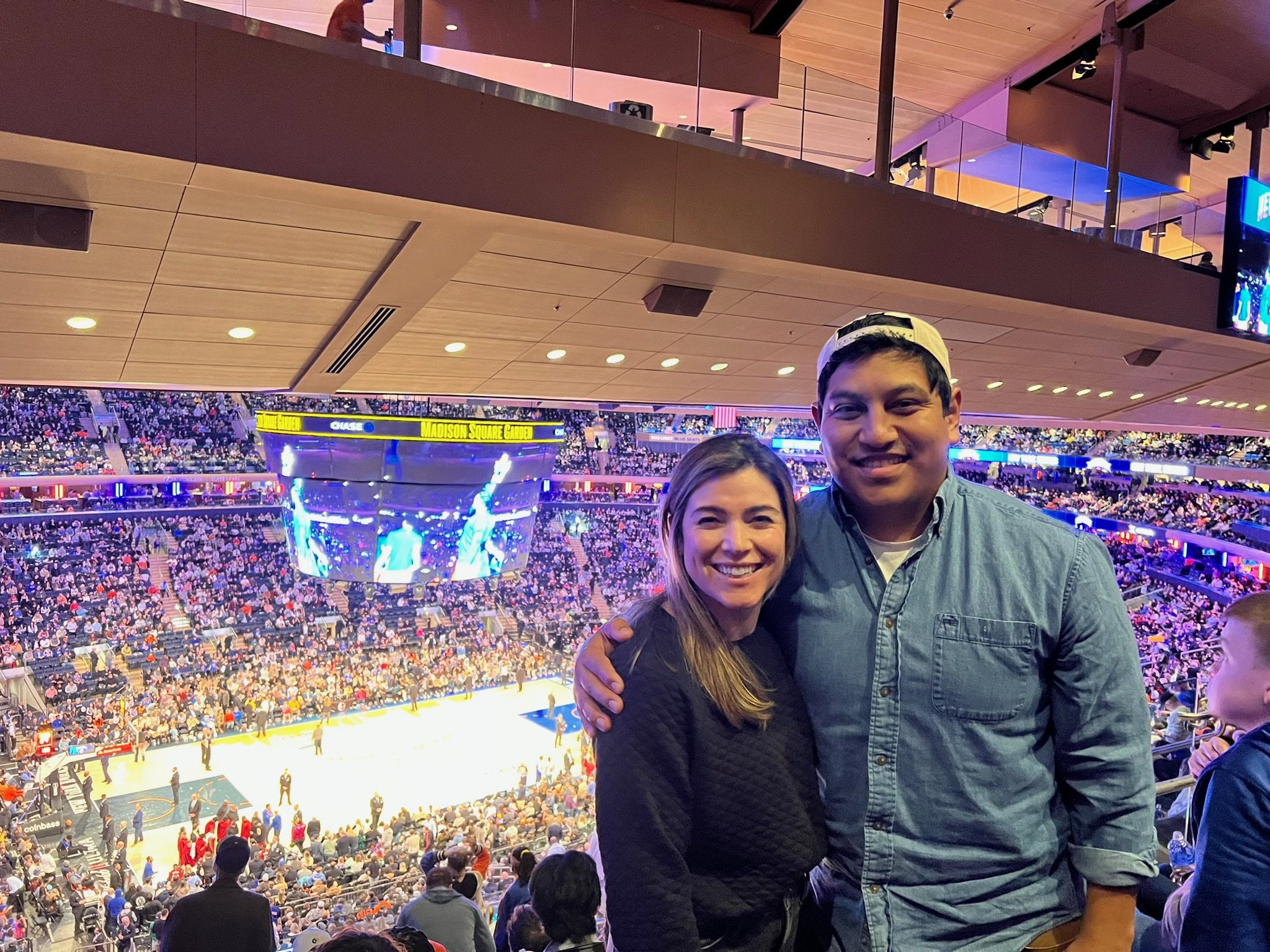People attending a basketball game in Madison Square Garden with a view from the balcony level, showing a large crowd on the court and the arena filled with spectators.