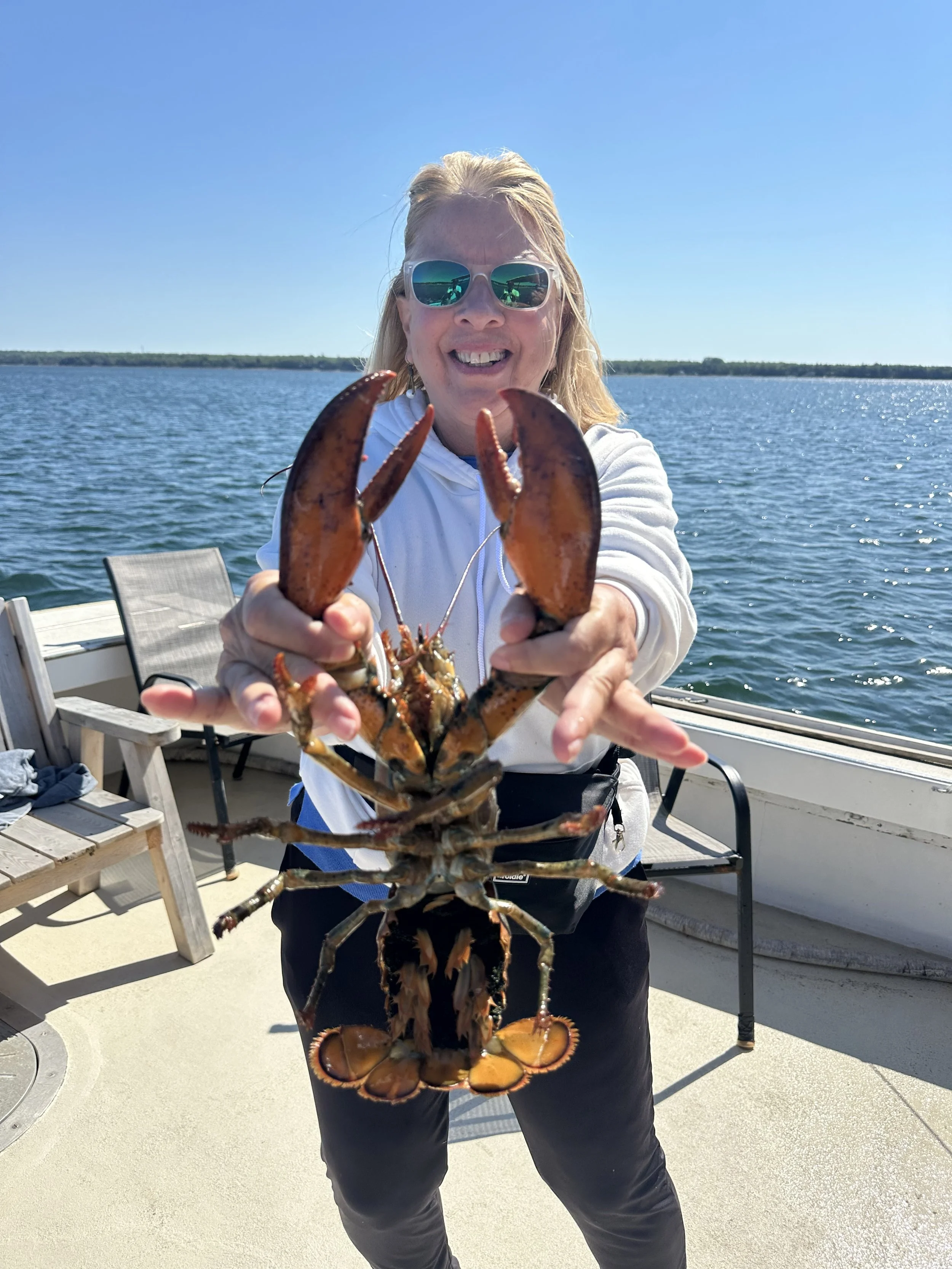 Becky Lynn-Crockford smiling on a boat on the Maine coast, holding a lobster.