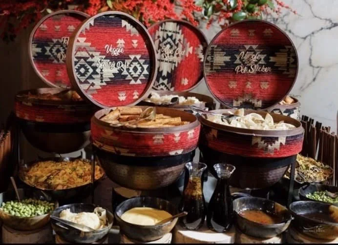 Colorful buffet of assorted dishes presented with patterned woven baskets.