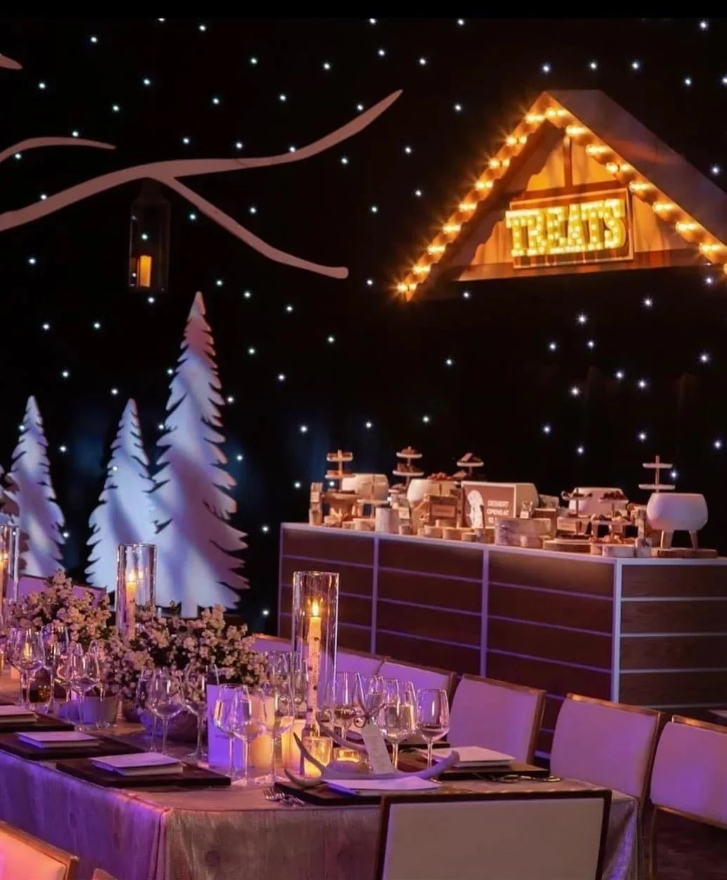 Candlelit dinner table in an immersive winter event setting with illuminated trees and stars.