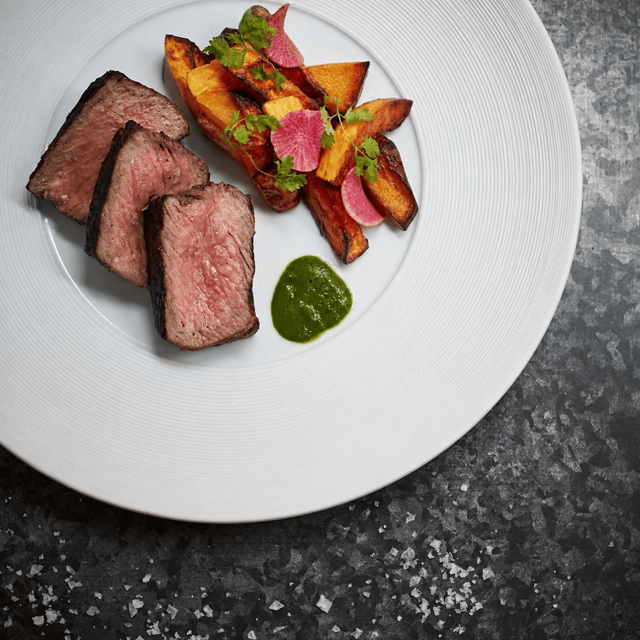 Medium-rare steak with roasted vegetables and green sauce.