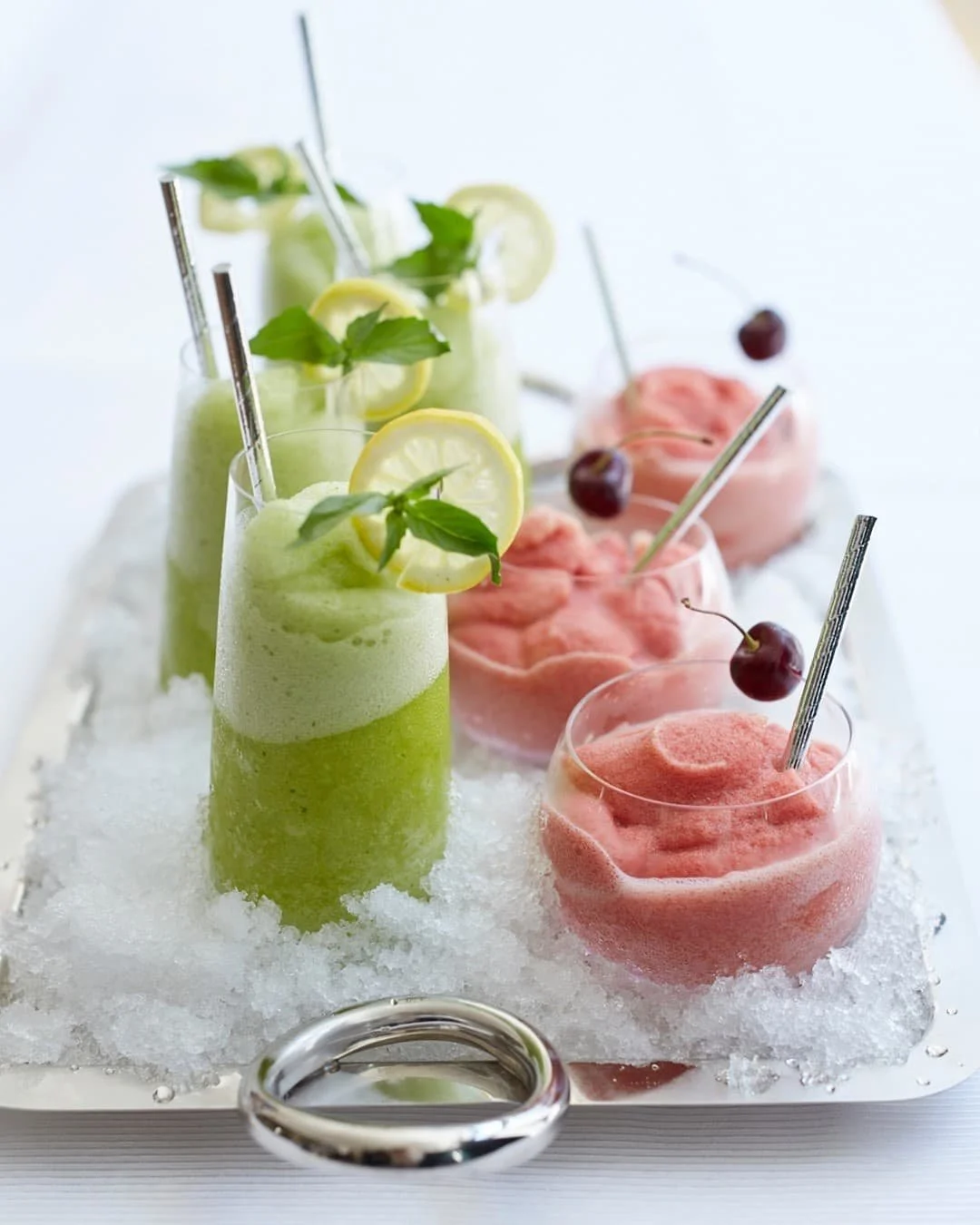 Green lime-mint and pink cherry frozen cocktails served over ice.