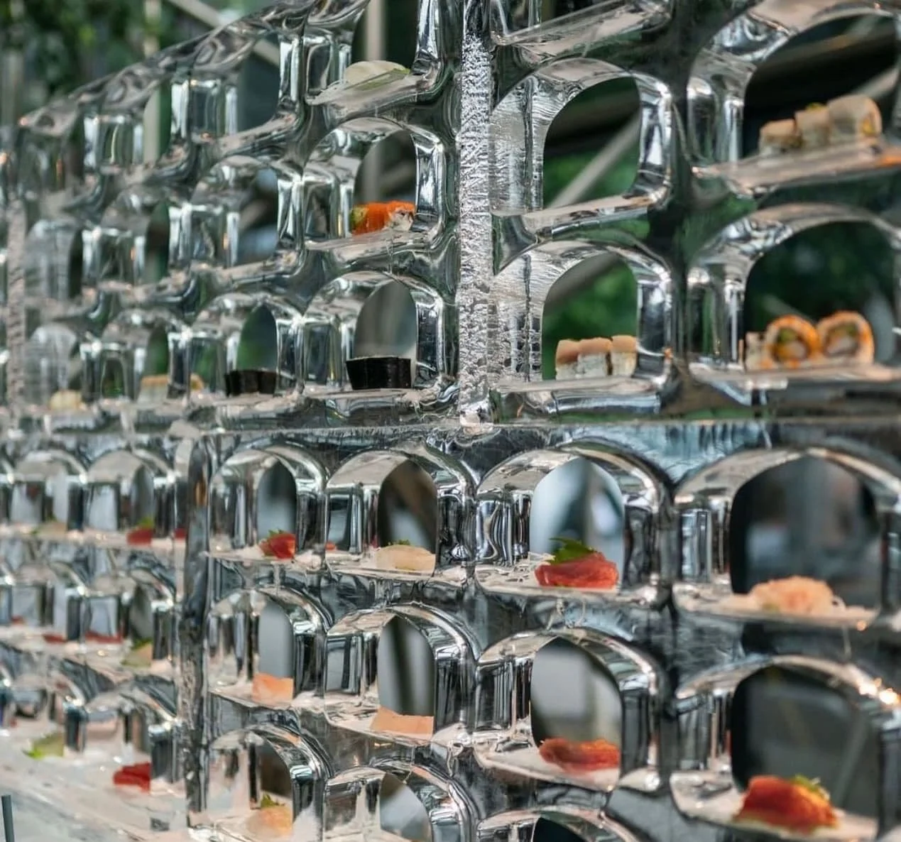 Modern tiered sushi display with individual pieces arranged on glass shelves.