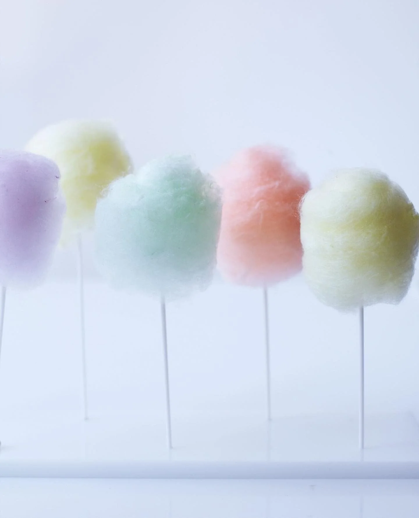 Pastel cotton candy bites arranged in a row on a reflective surface.