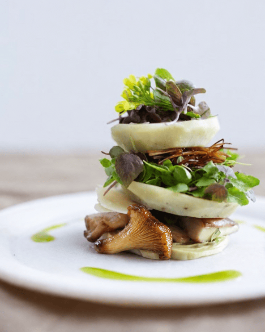 Layered vegetable course with microgreens and green sauce on a white plate.