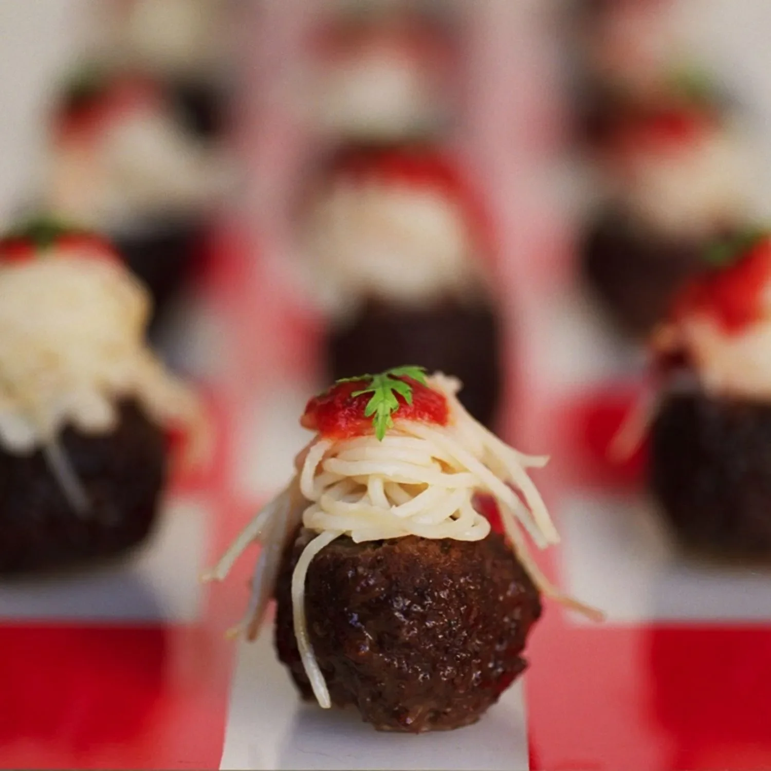 Miniature meatball hors d’oeuvre with red sauce and a fresh herb garnish.