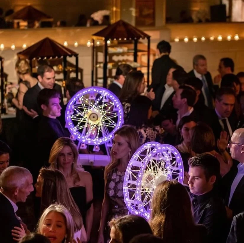Guests socializing at a large indoor event with illuminated Ferris wheel installations.