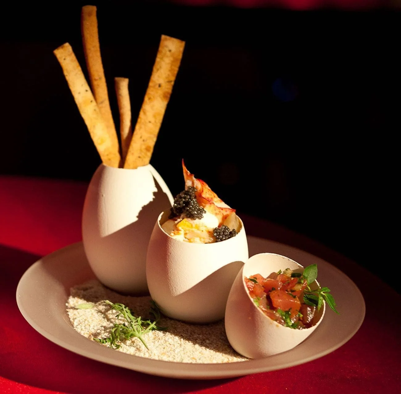 Gourmet bites served in eggshells with fresh herbs on a white plate.