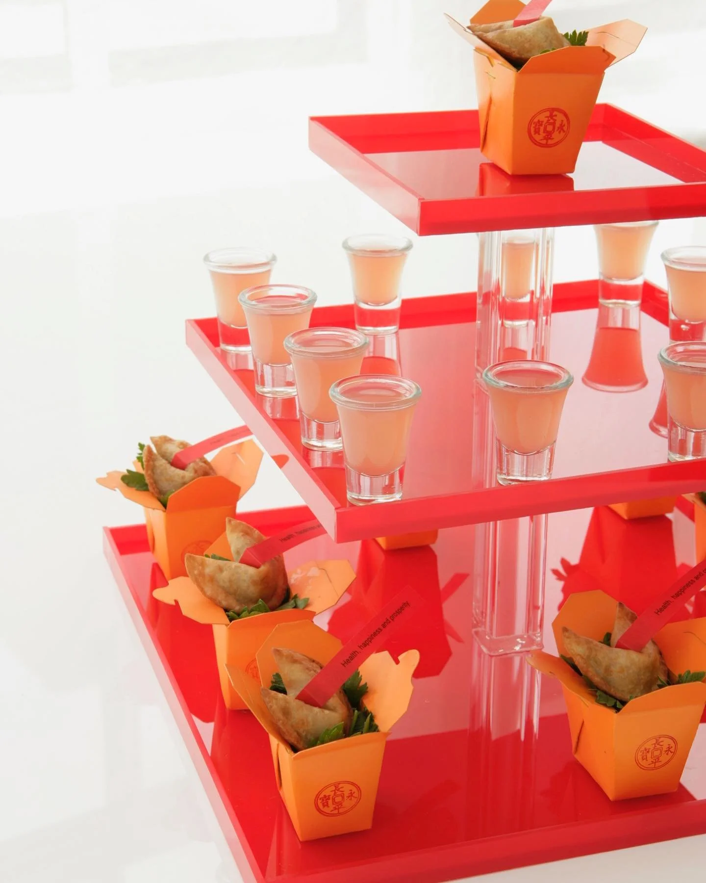 Spring rolls and peach-colored beverages arranged on a red tiered display.