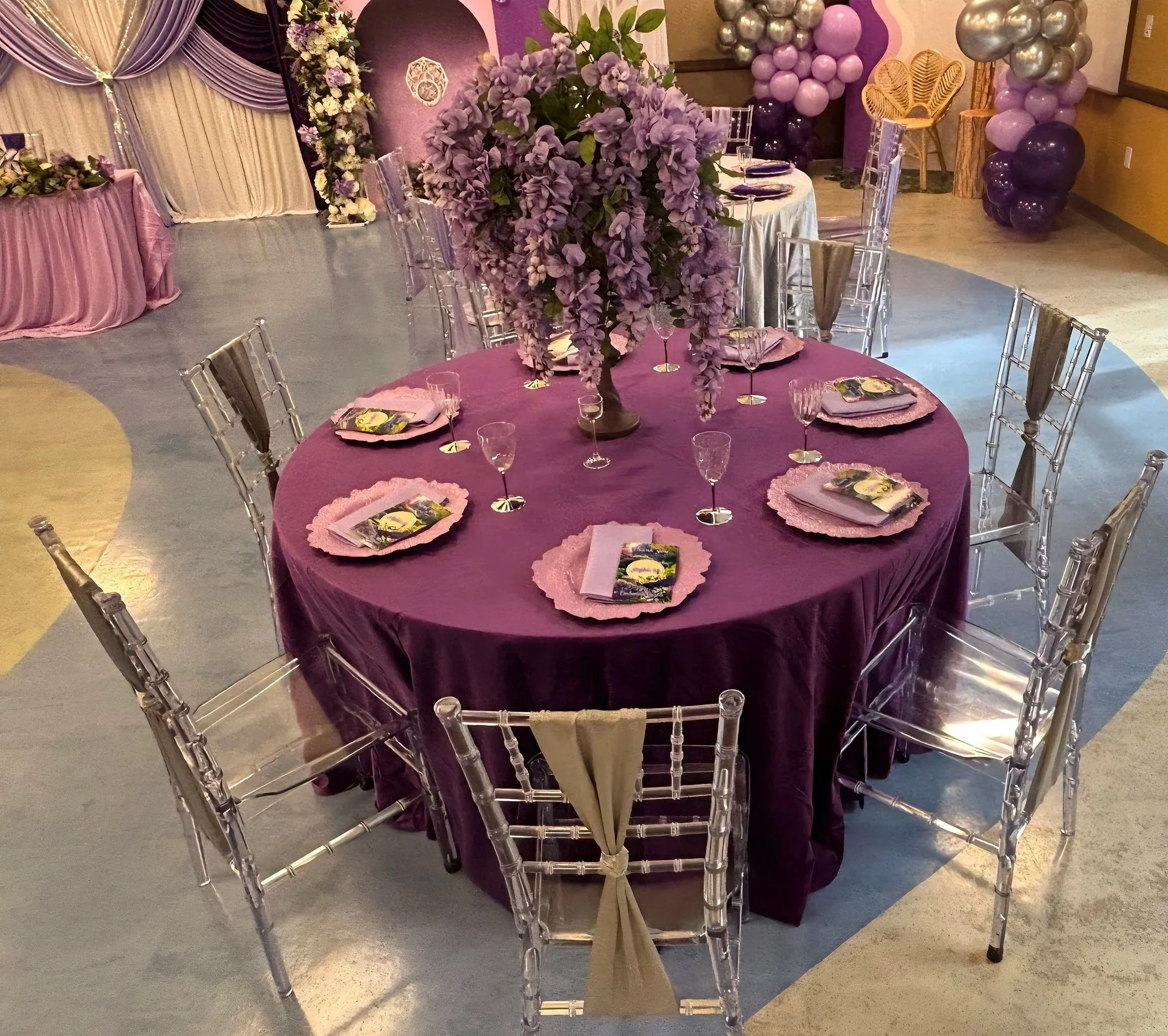 An Enchanted Sweet 16 brought to life with tree centerpieces, layered purple tones, and silver accents.   A life‑sized butterfly and a blooming garden backdrop complete this dreamy, storybook inspired celebration.