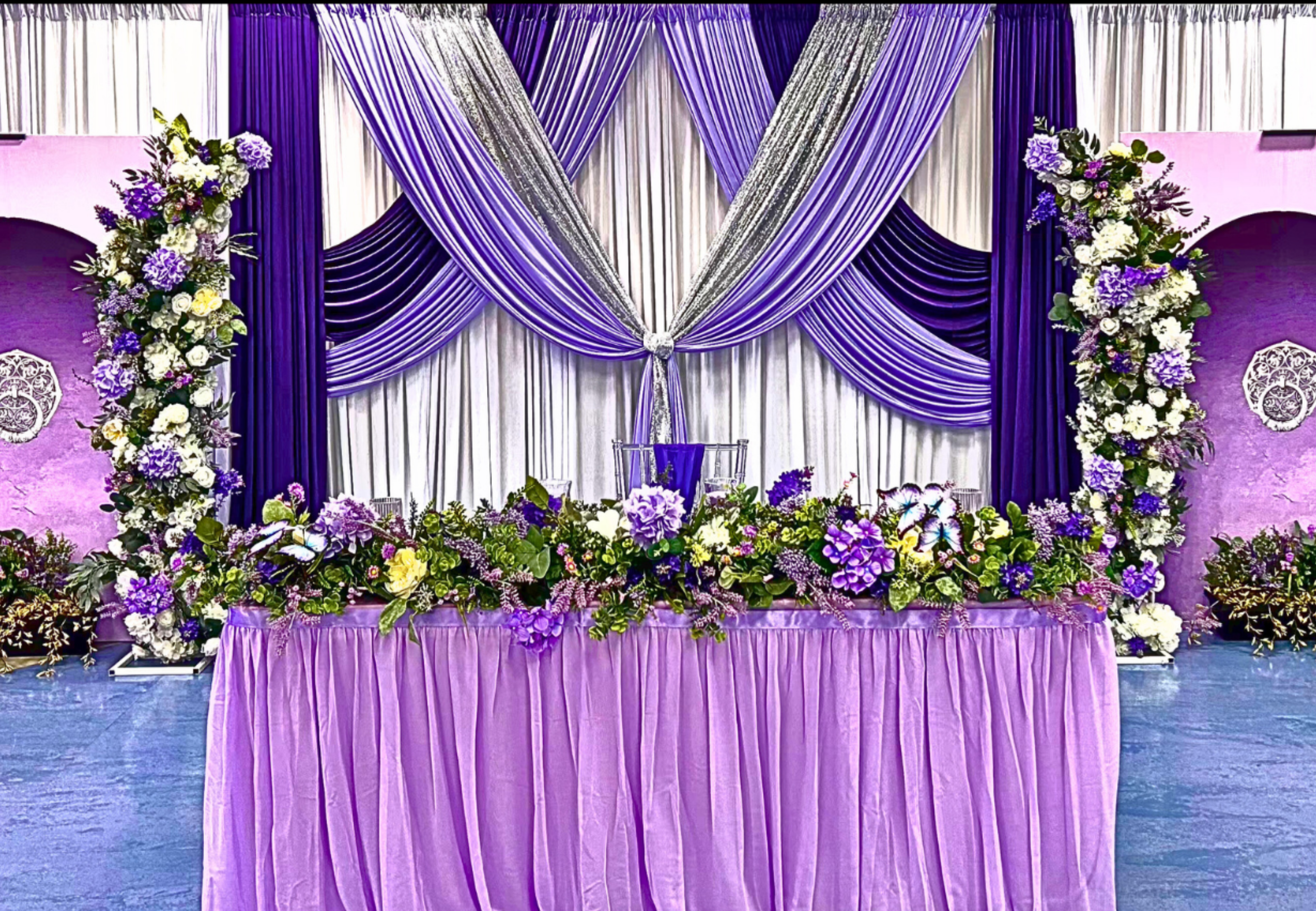 An Enchanted Sweet 16 brought to life with tree centerpieces, layered purple tones, and silver accents.   A life‑sized butterfly and a blooming garden backdrop complete this dreamy, storybook inspired celebration.