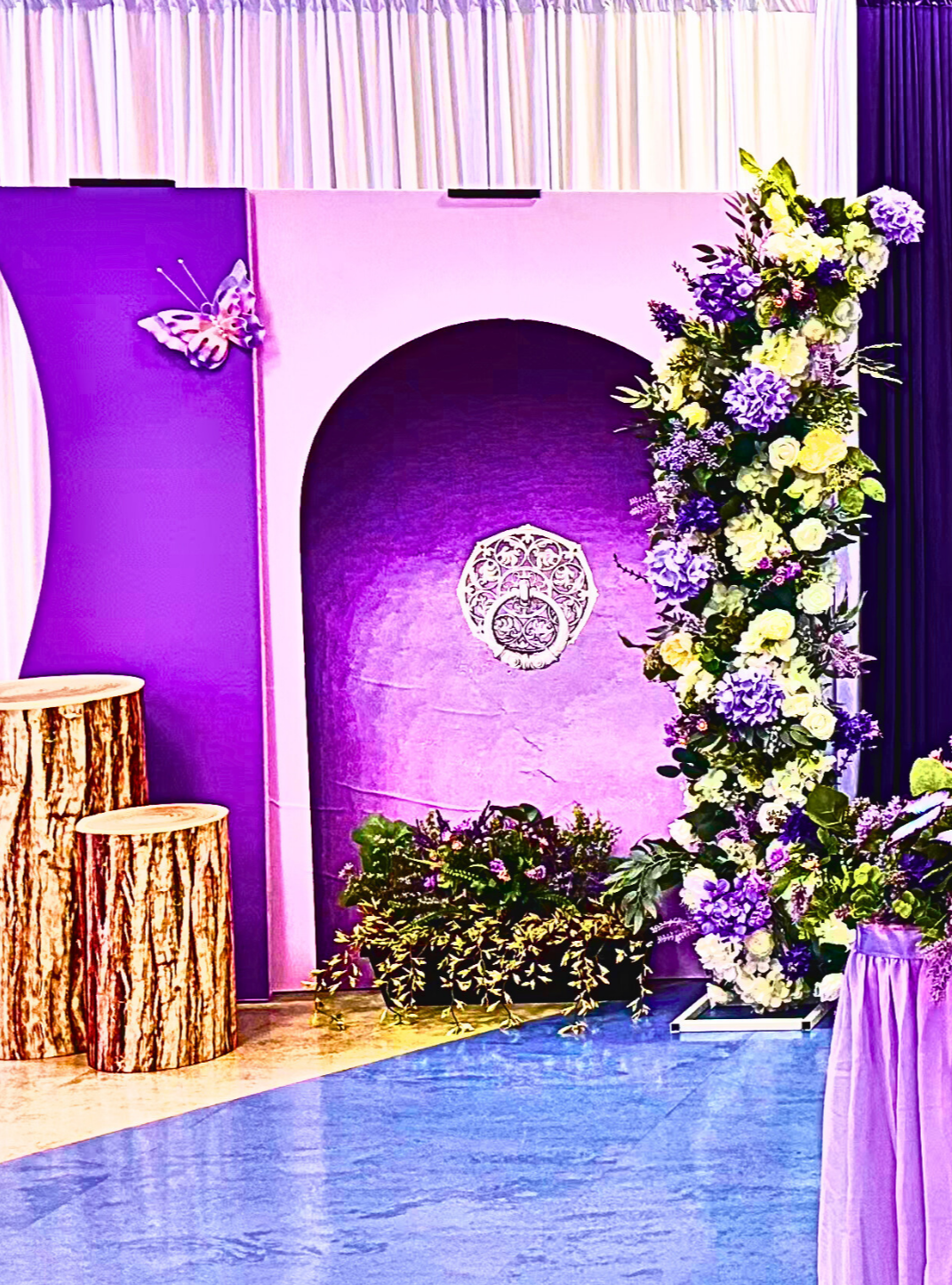 An Enchanted Sweet 16 brought to life with tree centerpieces, layered purple tones, and silver accents.   A life‑sized butterfly and a blooming garden backdrop complete this dreamy, storybook inspired celebration.