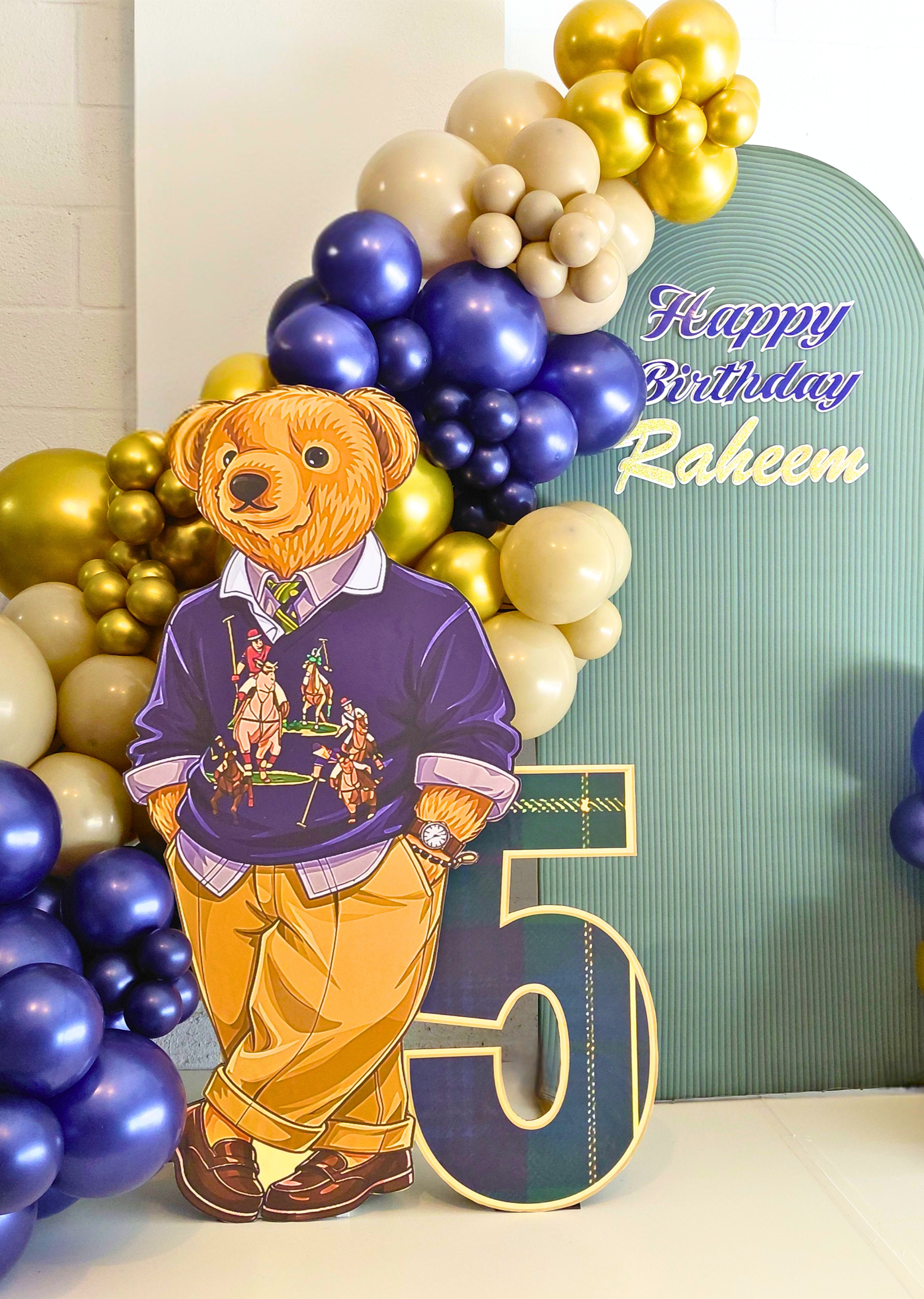A charming Teddy Bear–themed 5th birthday celebration designed with bold blue, tan, and gold color‑blocking.  A life‑sized bear, mini train, birthday hat, and number 5 prop highlight the theme and complete the cohesive look.