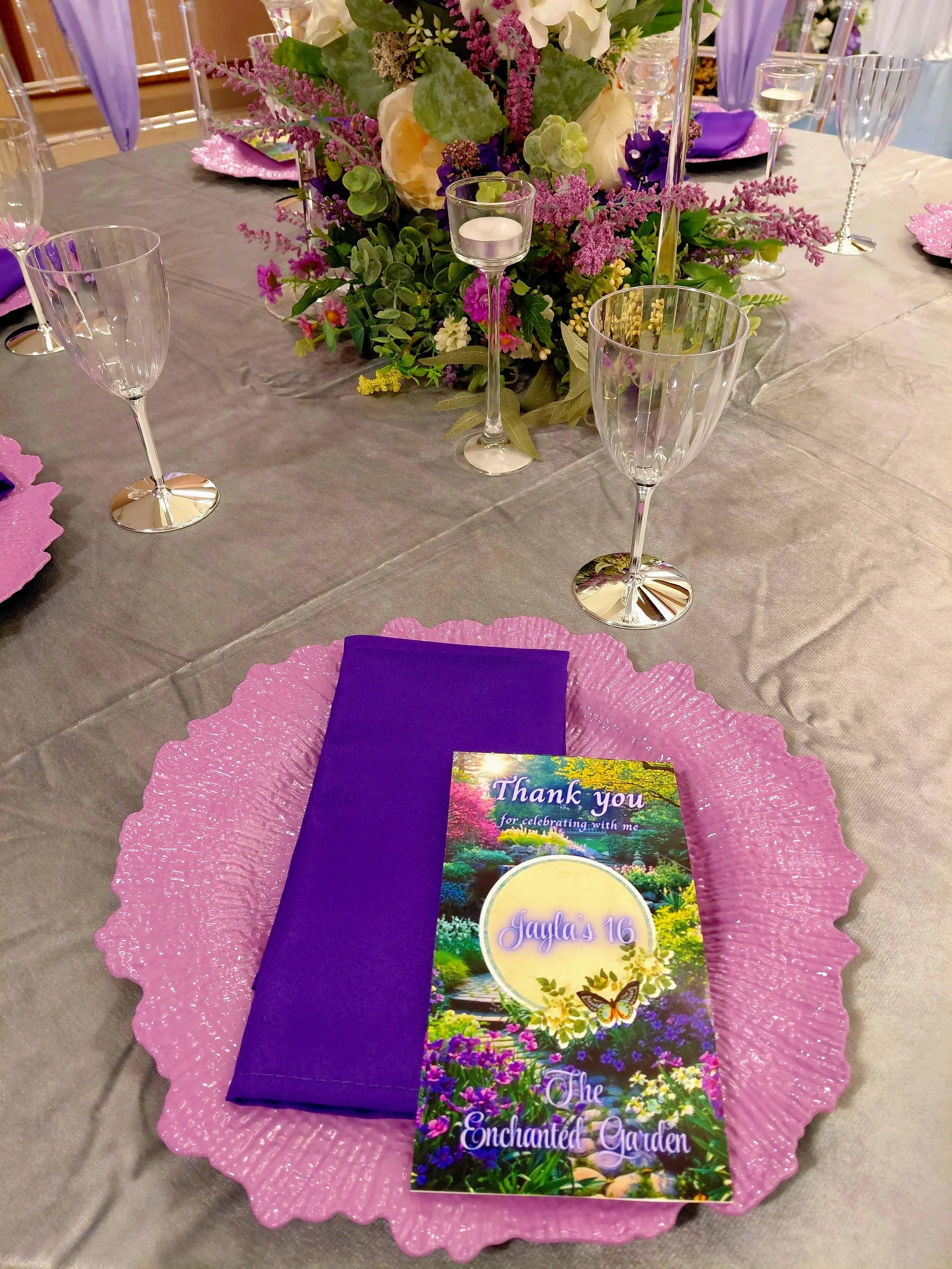 An Enchanted Sweet 16 brought to life with tree centerpieces, layered purple tones, and silver accents.   A life‑sized butterfly and a blooming garden backdrop complete this dreamy, storybook inspired celebration.