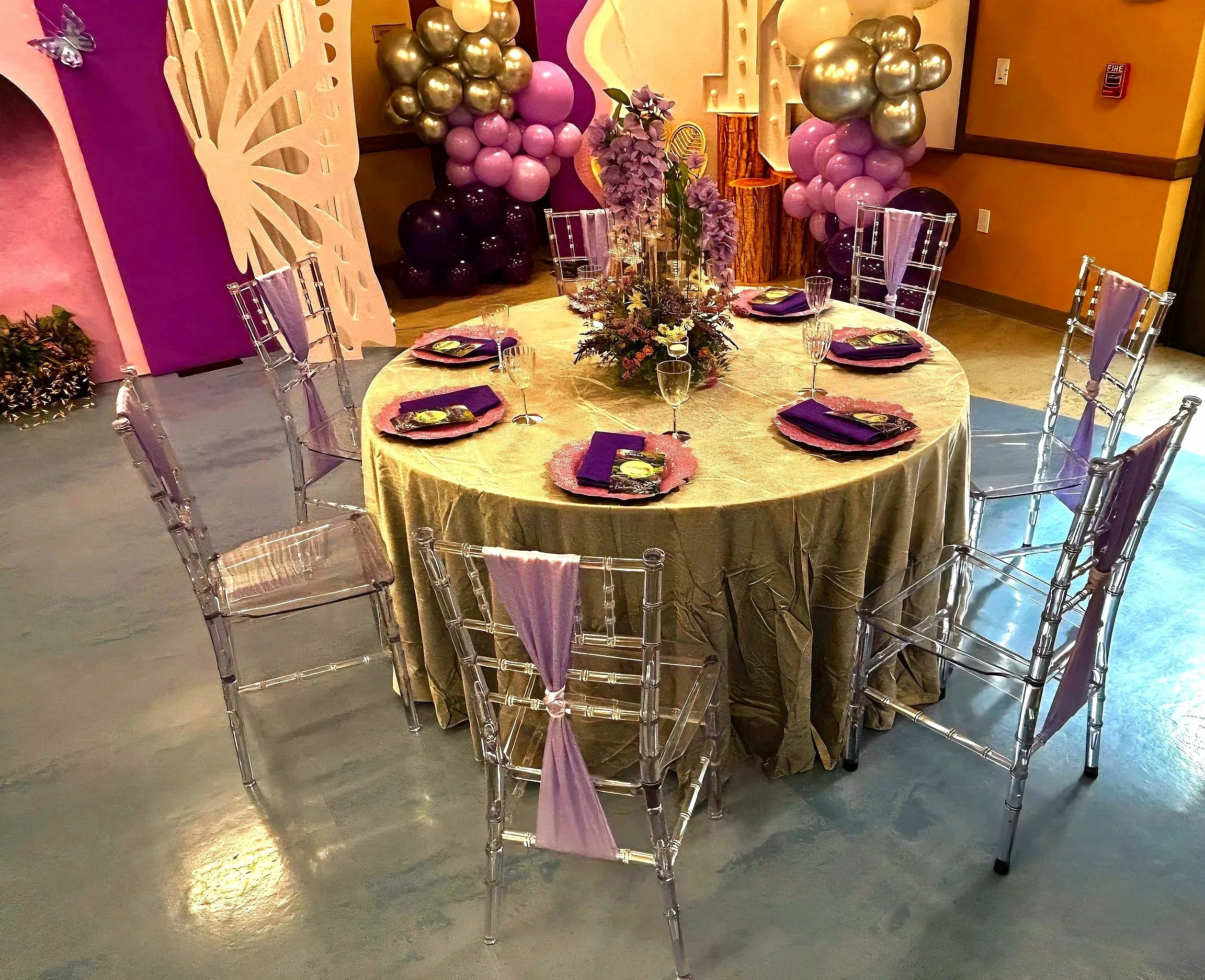 An Enchanted Sweet 16 brought to life with tree centerpieces, layered purple tones, and silver accents.   A life‑sized butterfly and a blooming garden backdrop complete this dreamy, storybook inspired celebration.