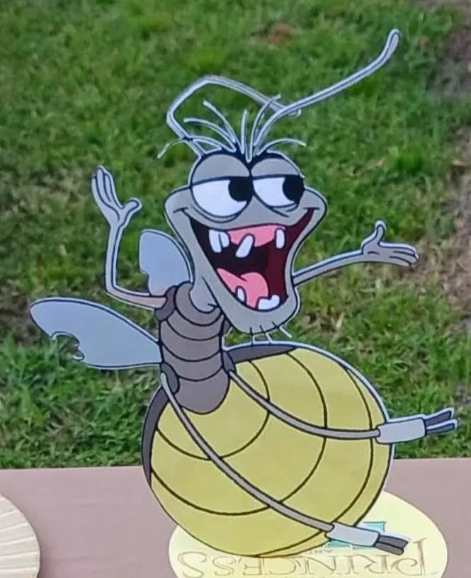 The Princess and the Frog cartoon illustration of a whimsical insect with a smiling face, large eyes, and a yellow segmented body, set outdoors on grass.