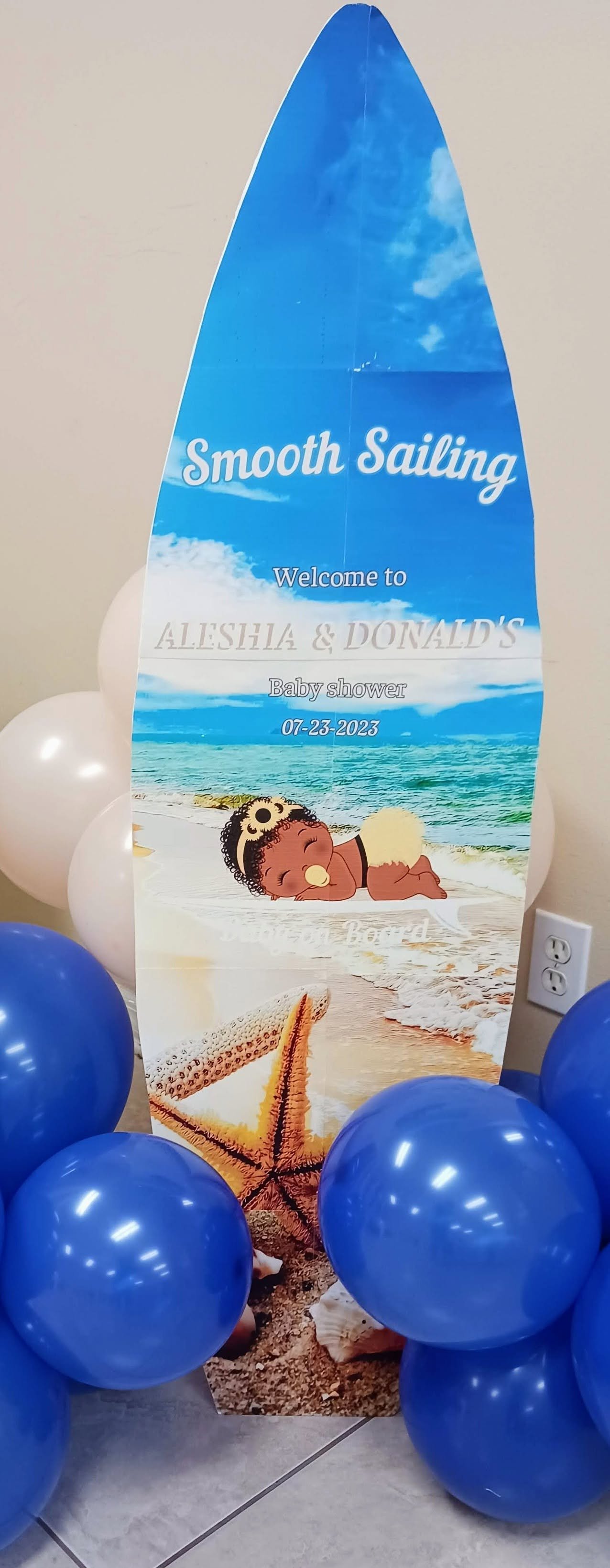 Surg-themed baby shower welcome sign with balloons.  The sign features a starfish, a baby sleeping on the beach, and a bright blue sky with clouds.