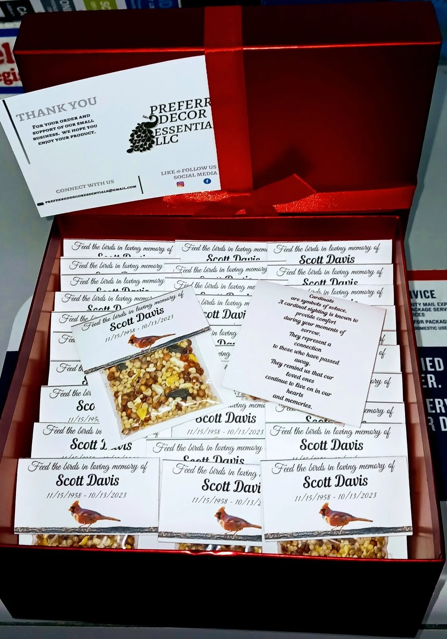 Open red box containing multiple memorial cards, with one card partially pulled out featuring a bird and a mix of seeds.
