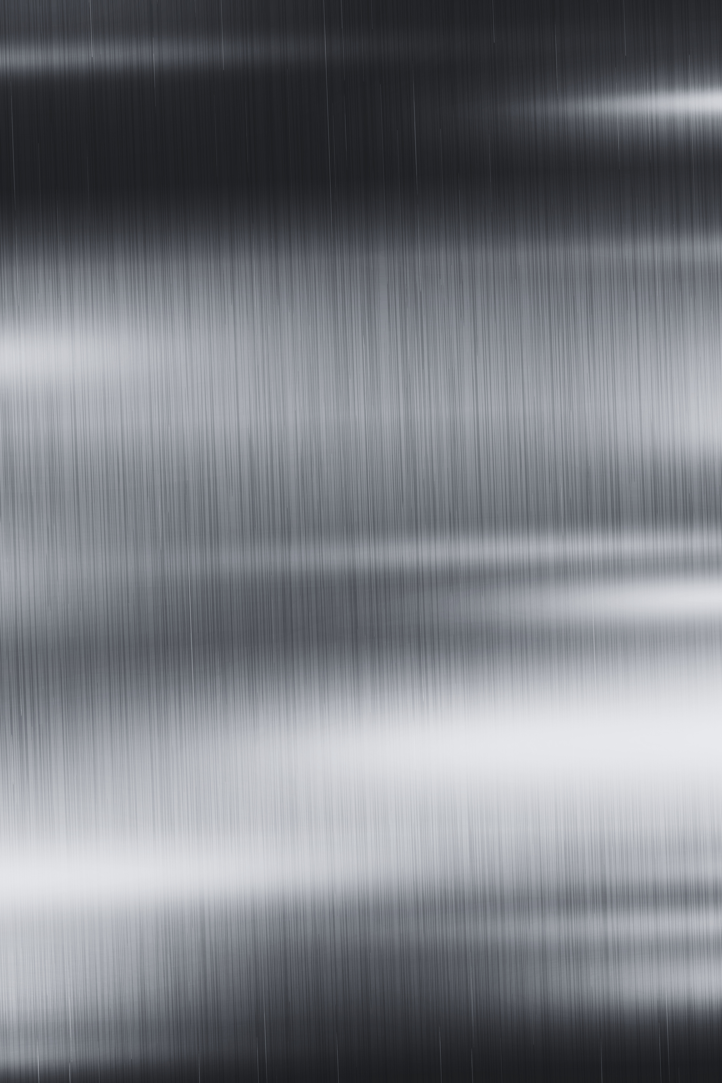 Blurred, metallic surface with vertical lines, appears to be a close-up of brushed stainless steel or similar material.