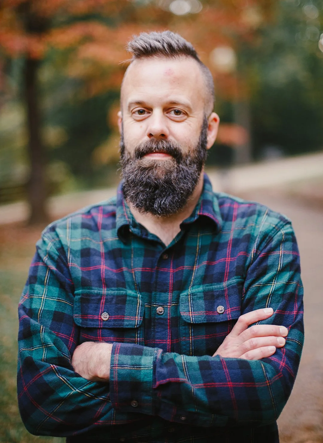 Brady Nicholson; owner of Dogwood Farm Designs; A man with a beard and short hair wearing a plaid green and blue shirt standing outdoors with trees in the background.