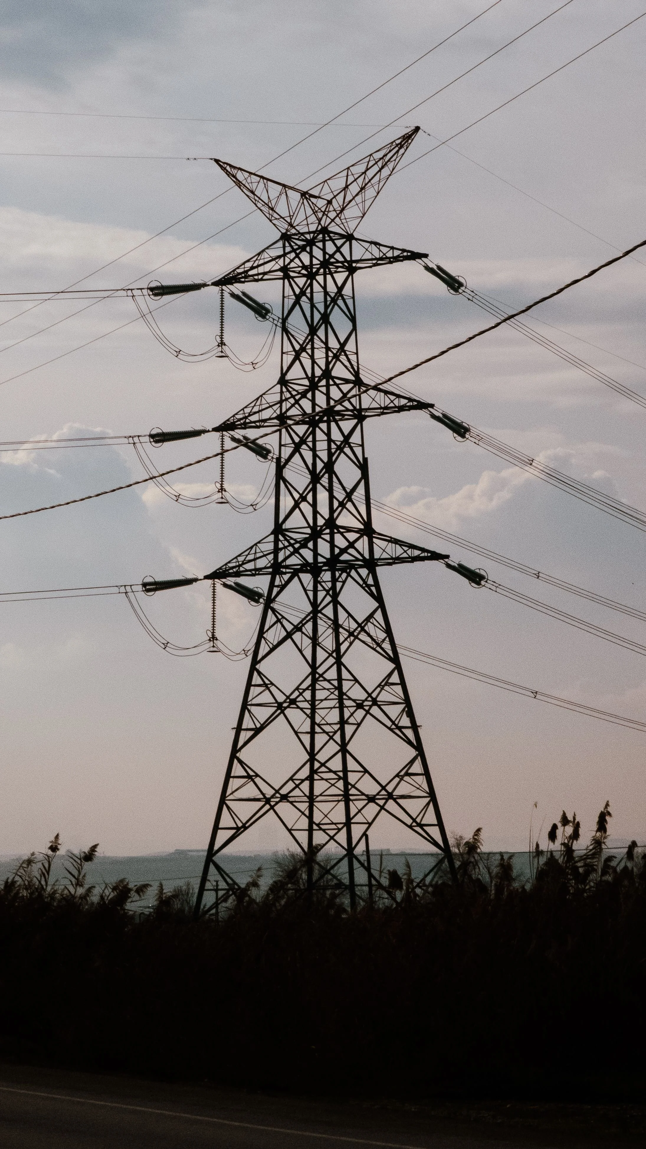 A large electrical transmission tower with power lines against a cloudy sky