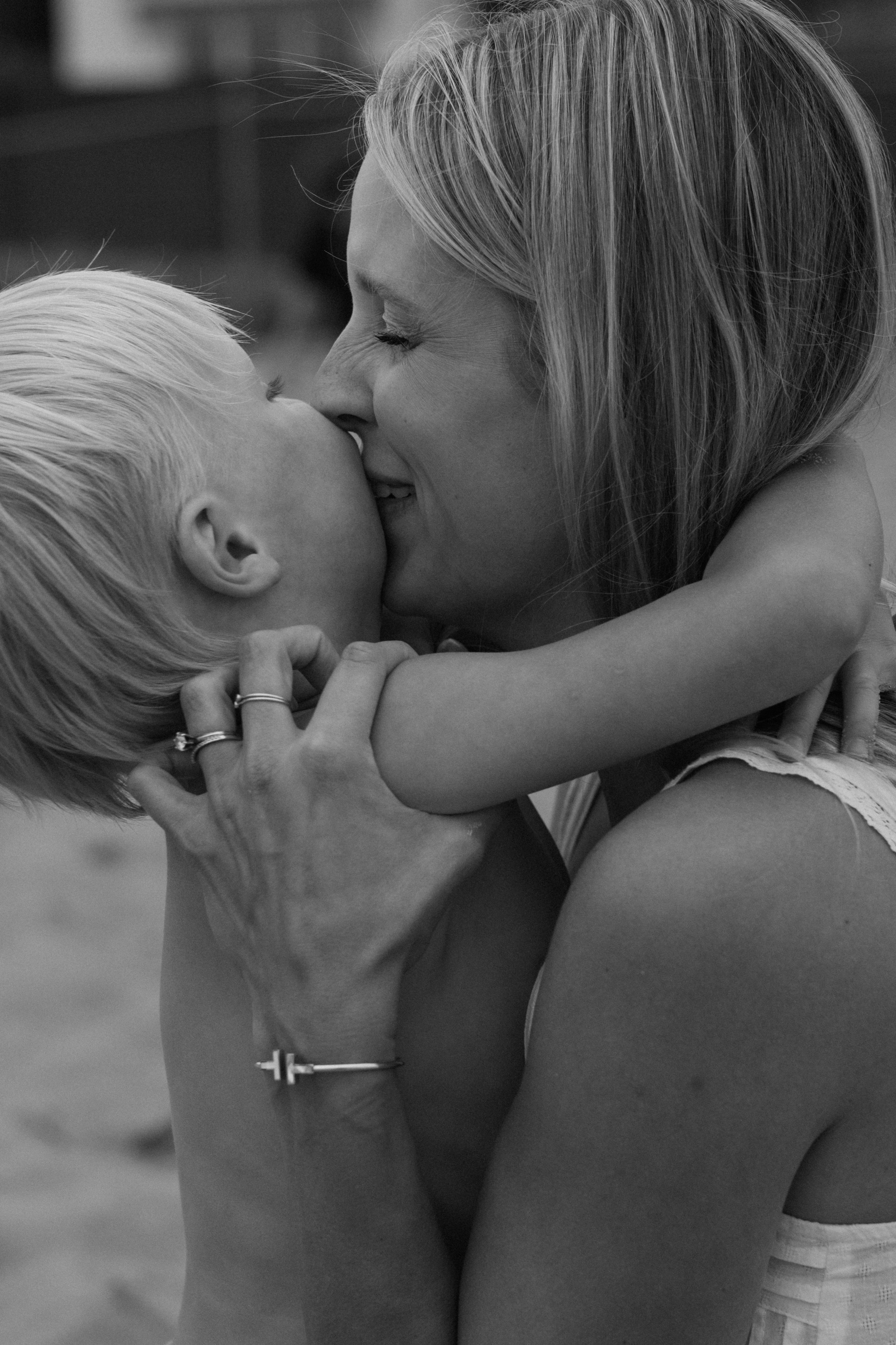 A woman and a young girl share a close, affectionate moment, with their faces touching and eyes closed, in a black-and-white photograph.