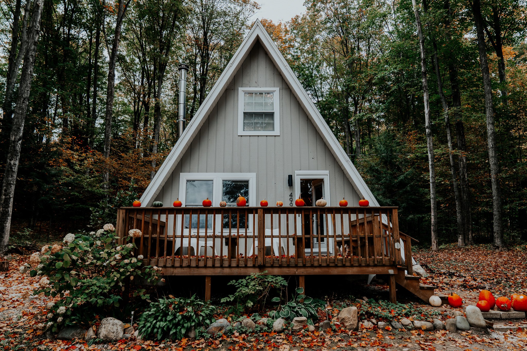 exterior photo of classic Aframe house in Michigan during the fall with changing leaves and pumpkins decorating the deck railing