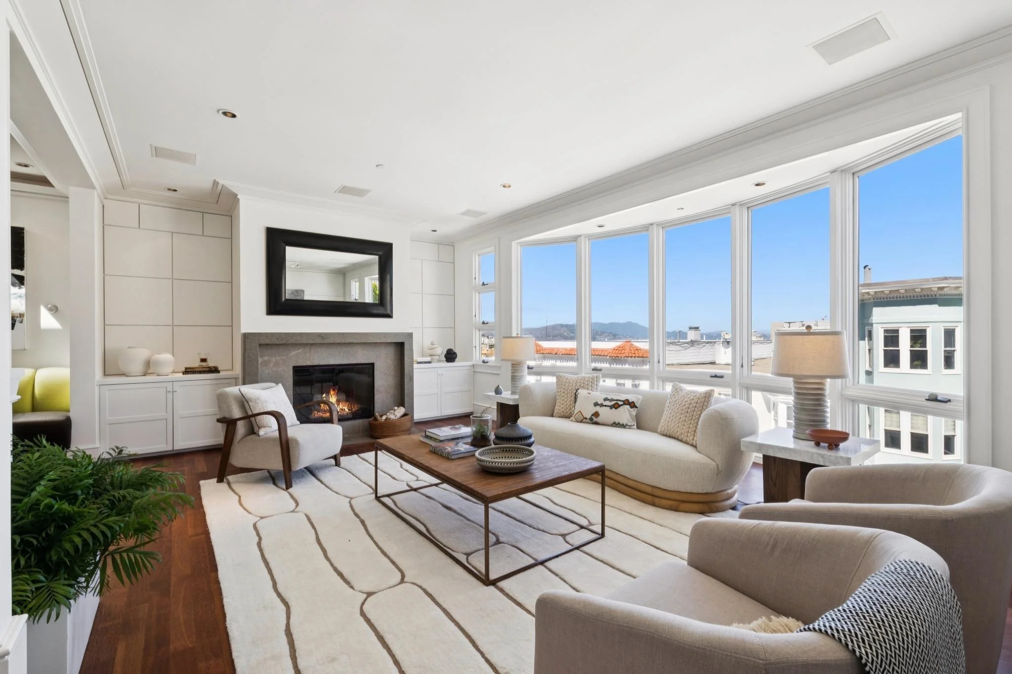 Bright living room with large window, white sofa, armchair, wooden coffee table, fireplace, and mountain view.