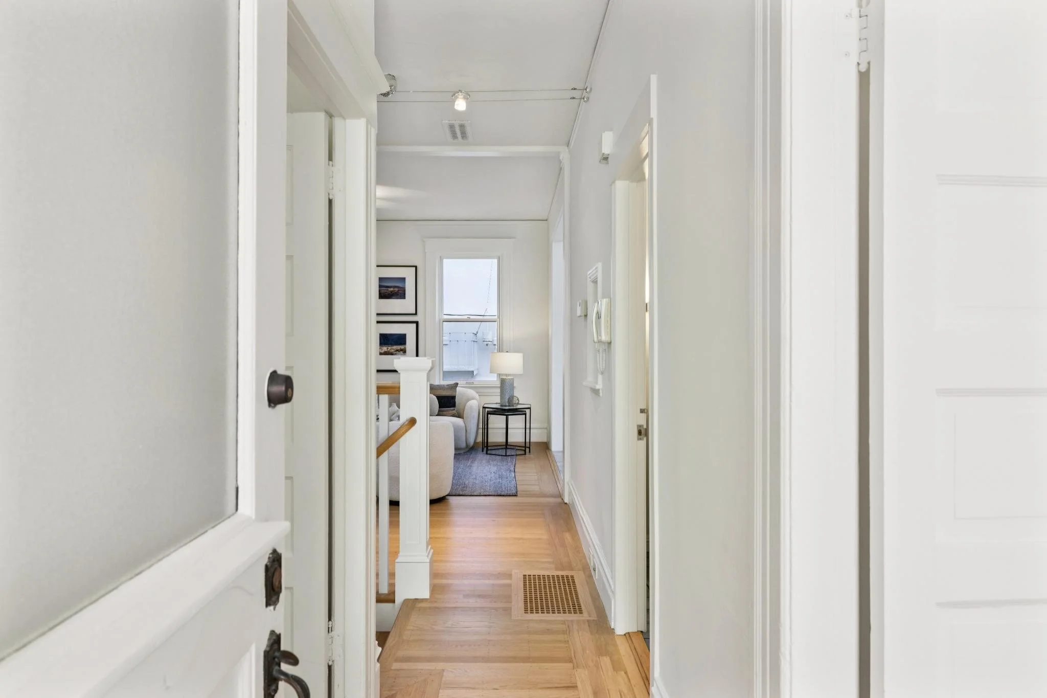 View from a front door looking into a bright living room with hardwood floors, white walls, and framed pictures on the wall.