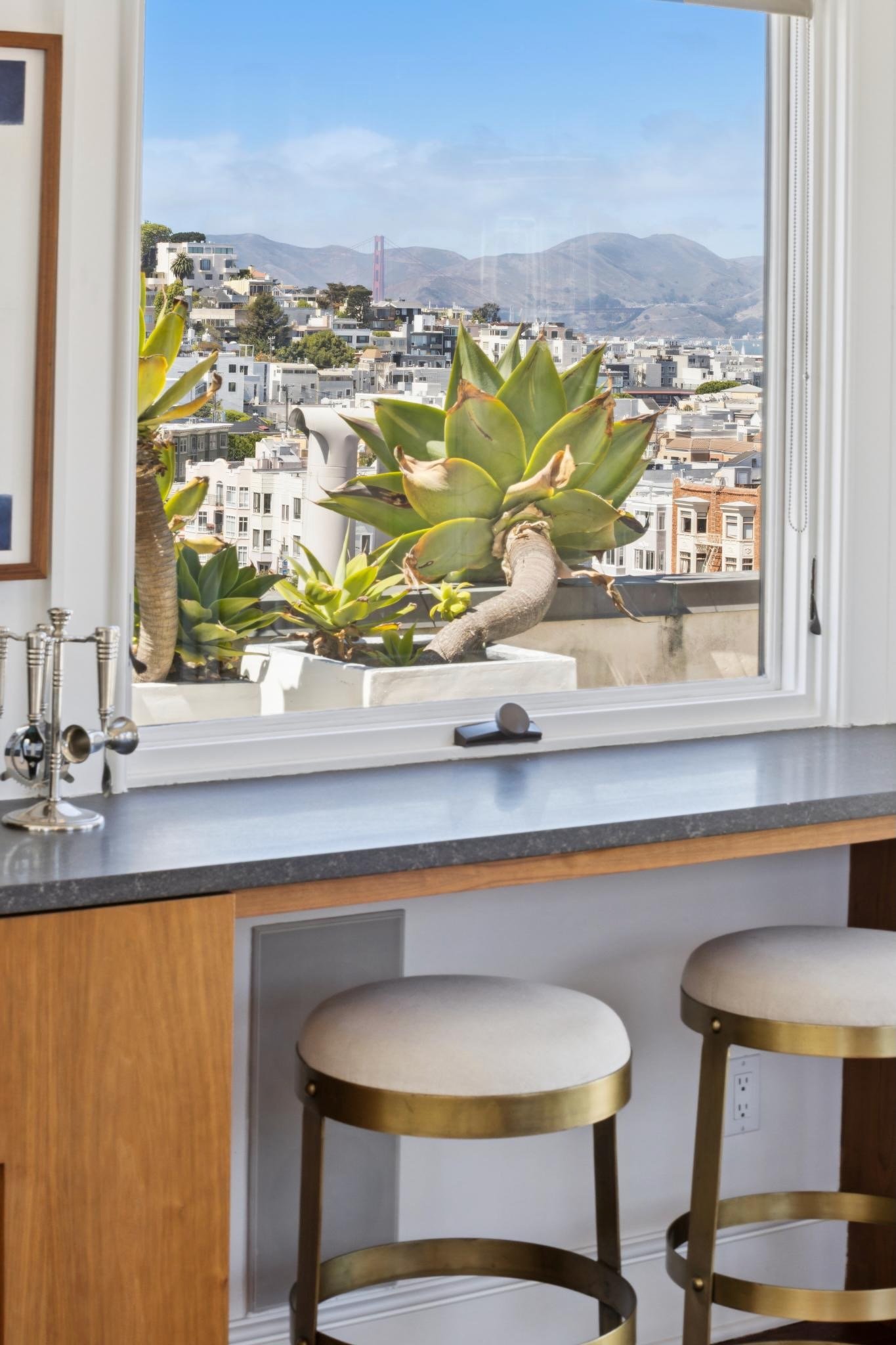A kitchen window with a view of San Francisco, California, including the Golden Gate Bridge and hilly cityscape, with potted succulents on the windowsill.