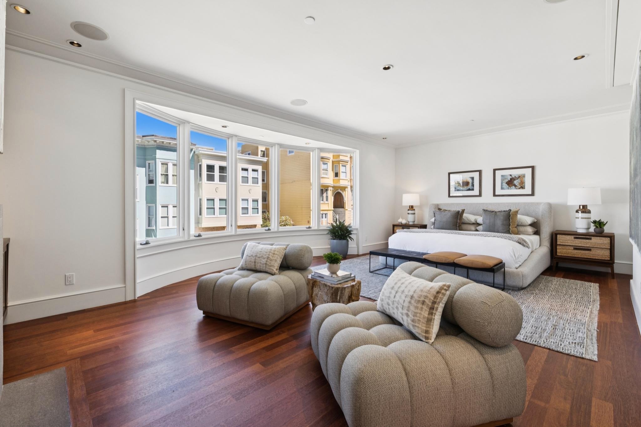 Modern living room with large bay window, white walls, wood flooring, and contemporary furniture, including a sofa, armchair, and coffee table.