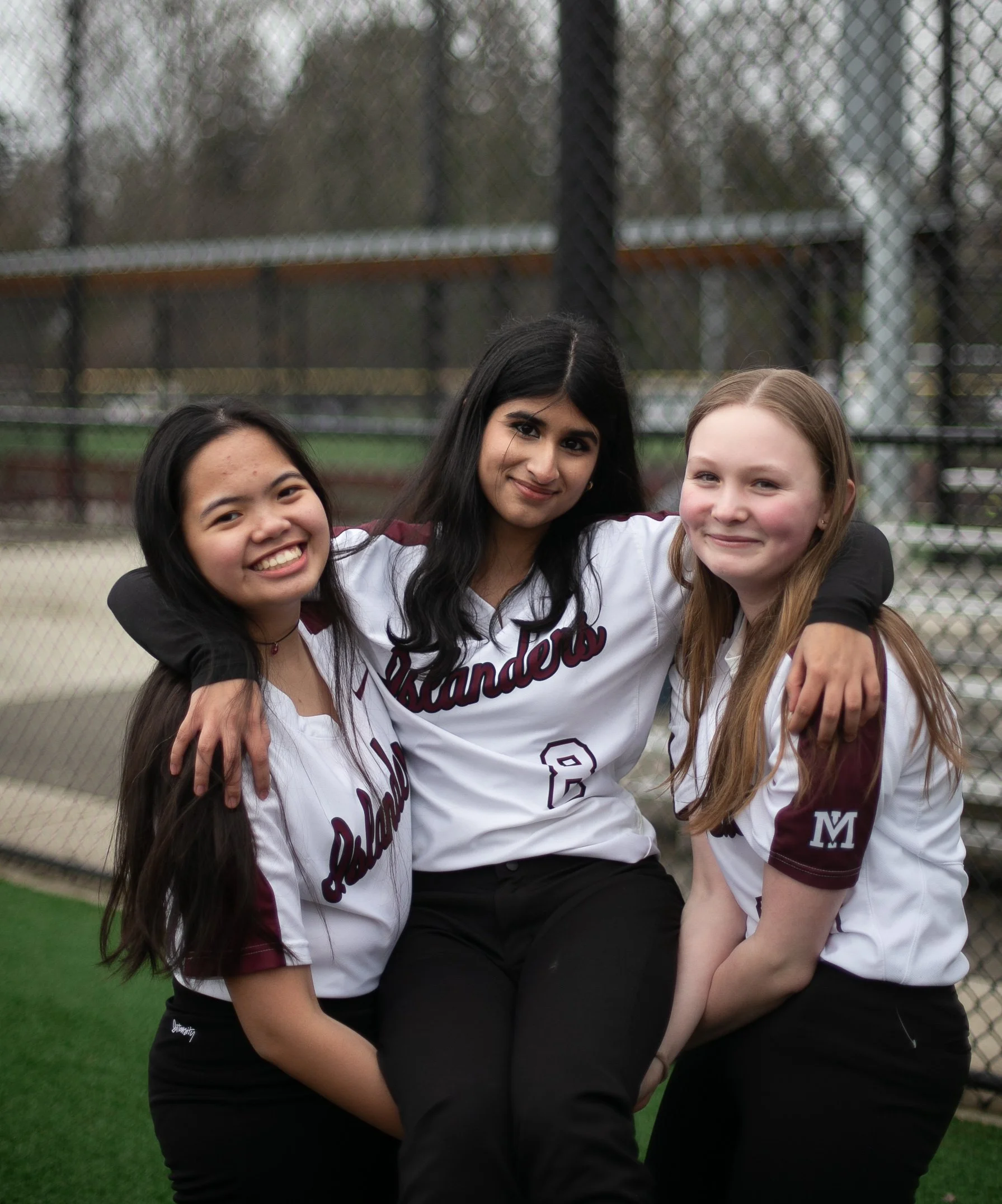 Three Mercer Island softball teammates pose beside the fence.