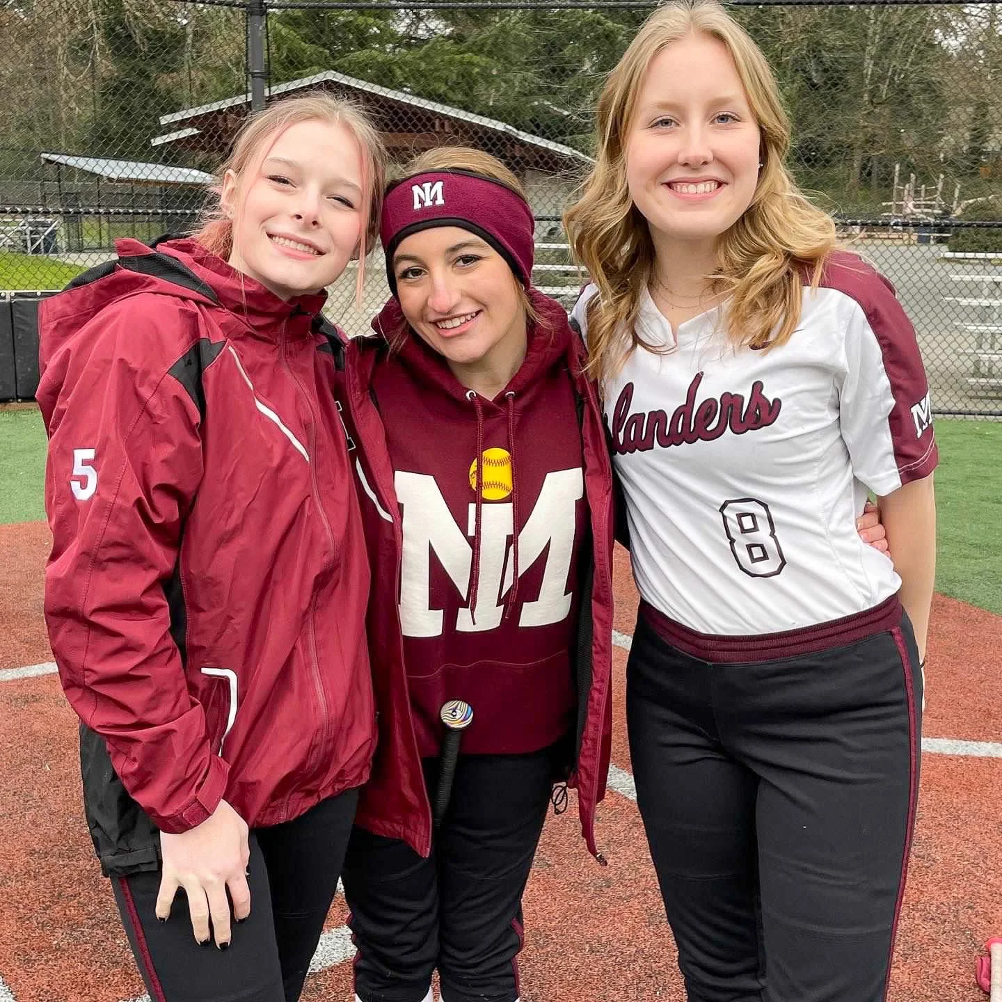 Three MIHS softball teammates smile together near the field.