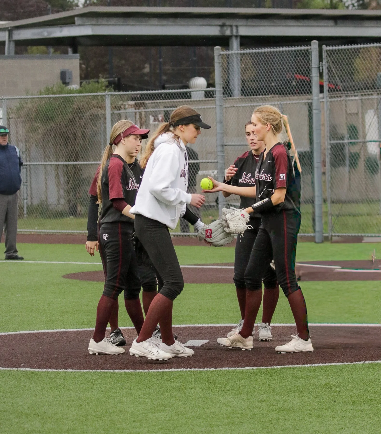 Coach meets with Mercer Island softball players on the infield.