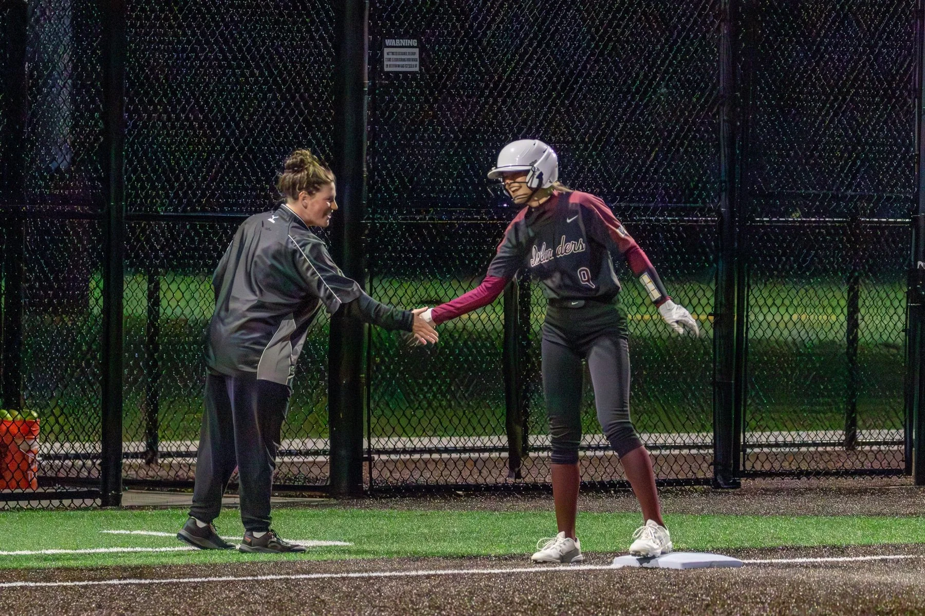 Softball players exchange a handshake on the field at night.