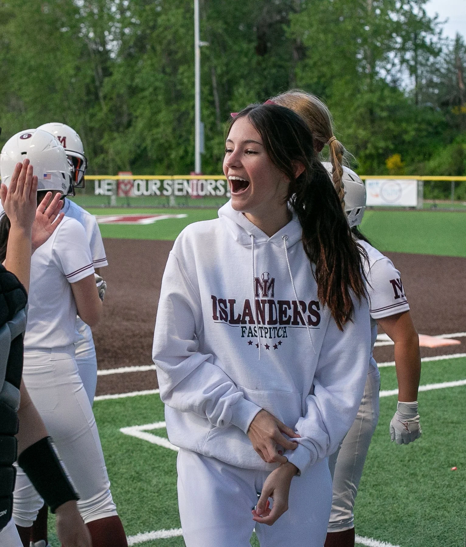 MIHS softball teammates laugh together beside the field.