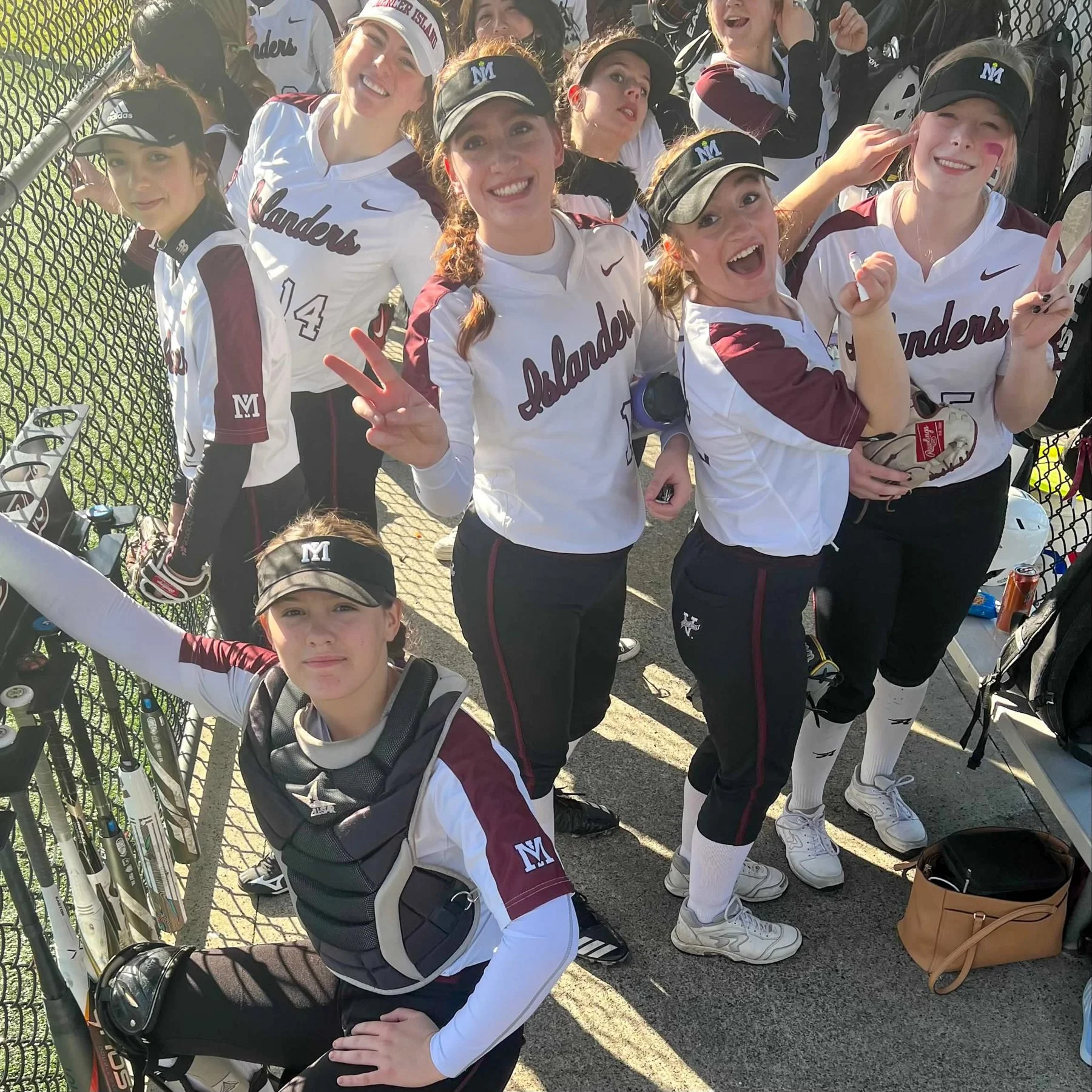 MIHS softball teammates smile and wave beside the dugout.