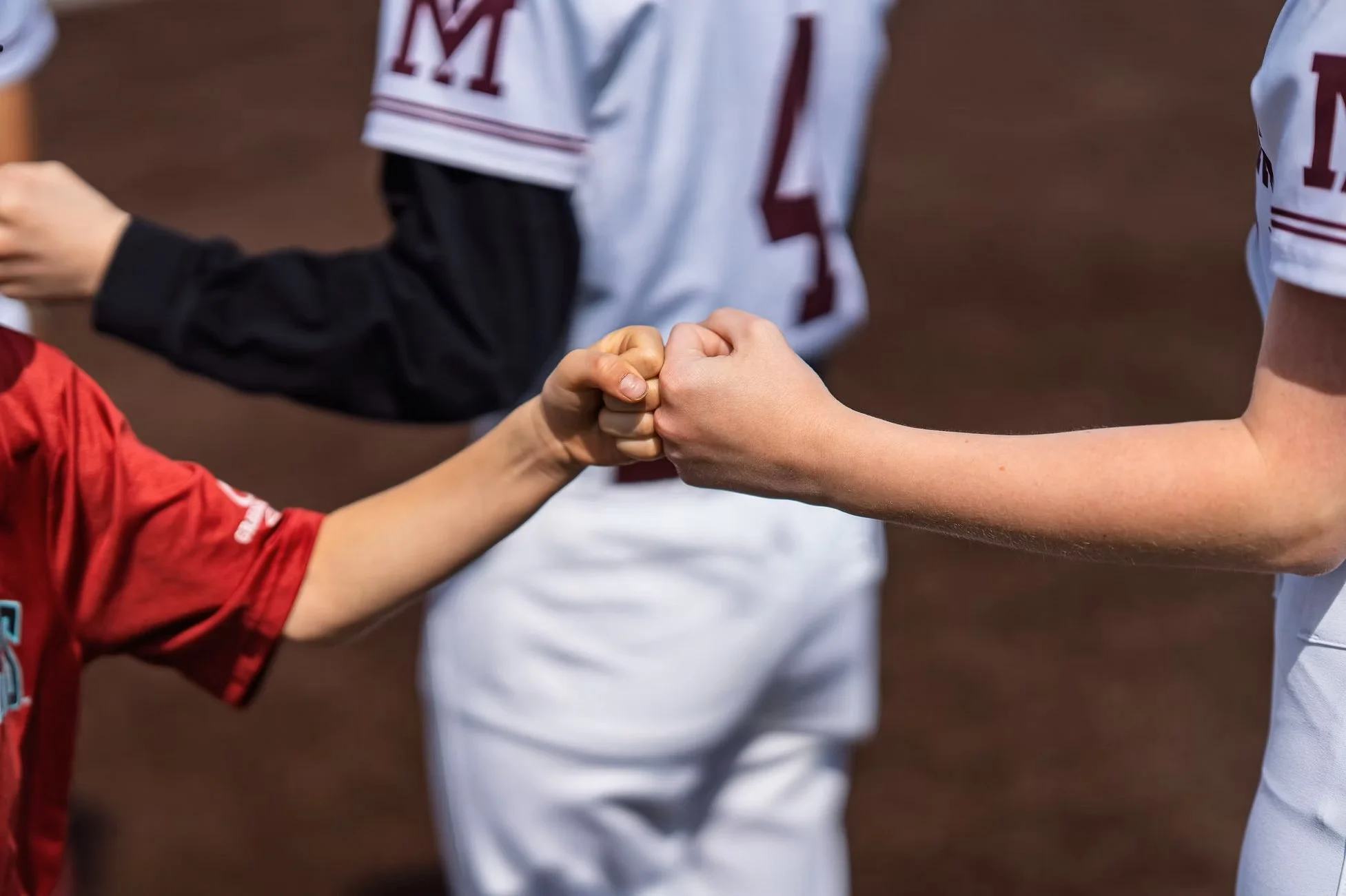 Softball players exchange a fist bump on the field.