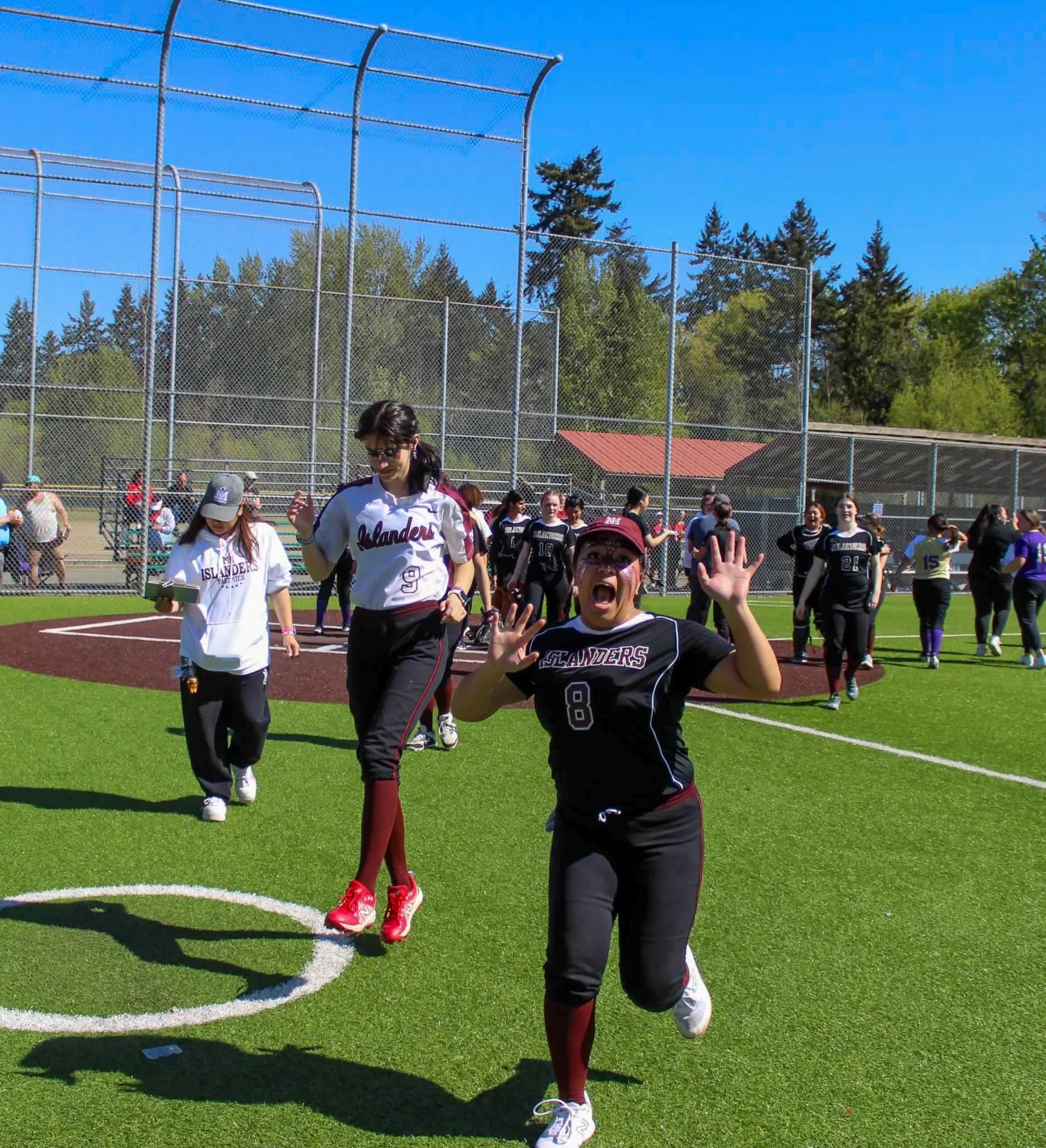 Islander softball players run toward the camera with hands raised.
