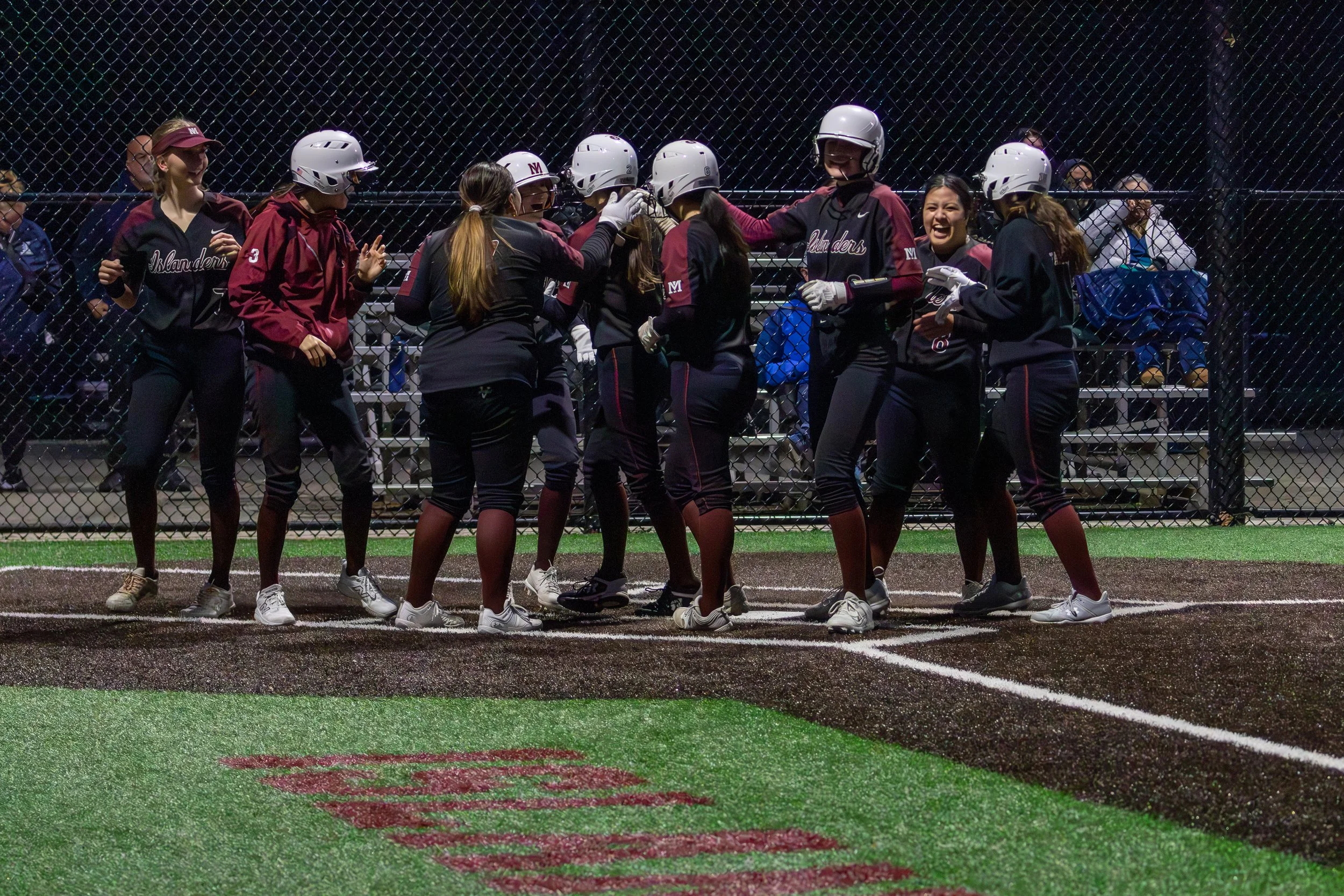 MIHS softball teammates gather at home plate during a night game.