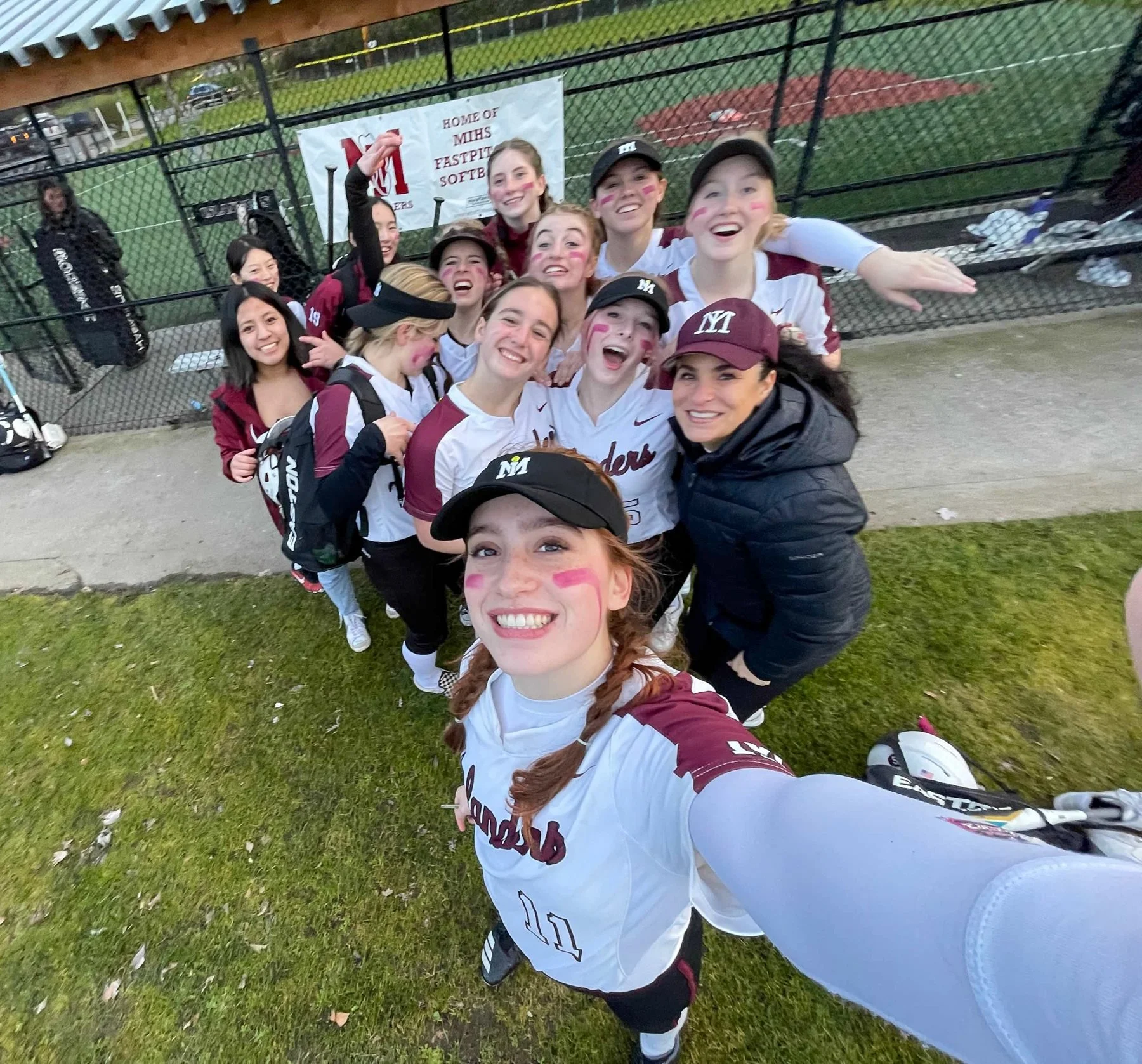 MIHS softball teammates take a group selfie beside the dugout.